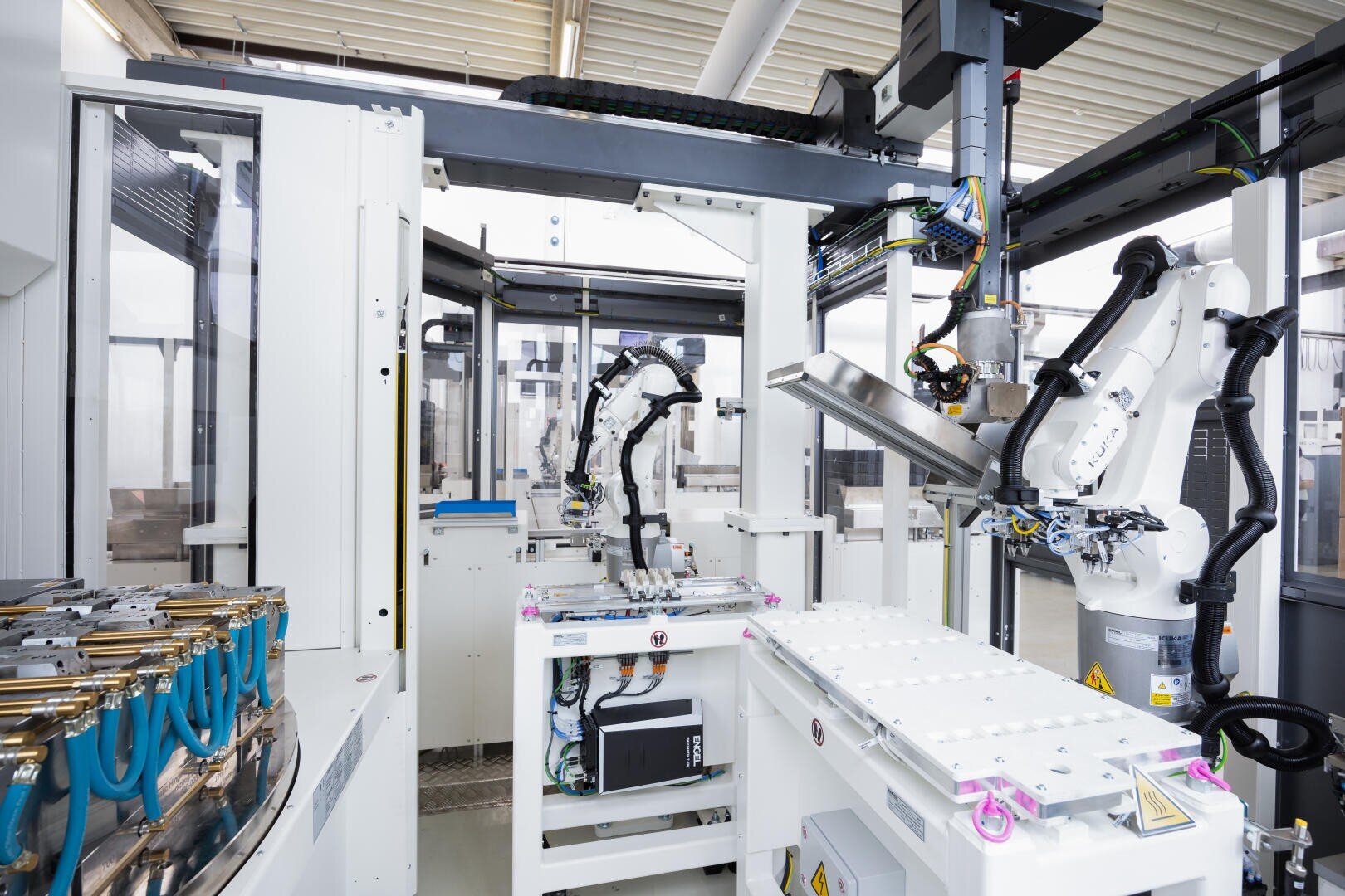 A modern manufacturing plant with robotic arms and automated machines assembling or handling components on a production line, surrounded by white industrial equipment.
