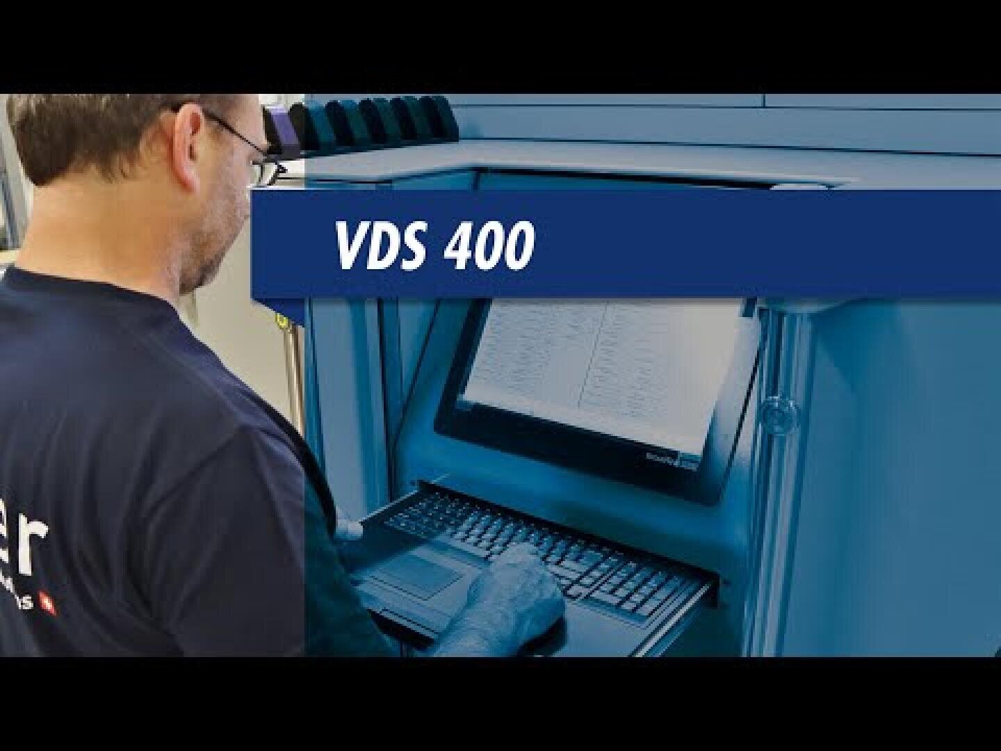 Eine Person, die eine Brille und ein dunkles Hemd trägt, bedient einen Computerarbeitsplatz mit der Bezeichnung VDS 400, liest Daten auf einem Monitor und tippt auf einer Tastatur in einer technischen oder industriellen Umgebung.