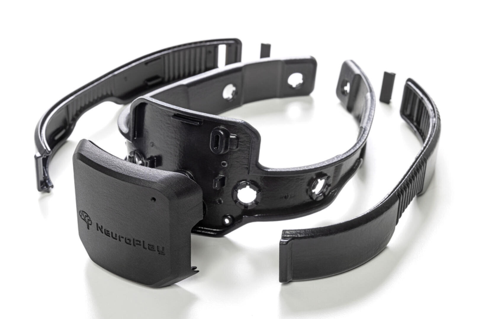 Ein schwarzes, modulares elektronisches Headset mit abnehmbaren Teilen ist auf weißem Hintergrund abgebildet. Der Hauptteil ist mit Neuroplay beschriftet und weist kleine Öffnungen und Anschlüsse auf.