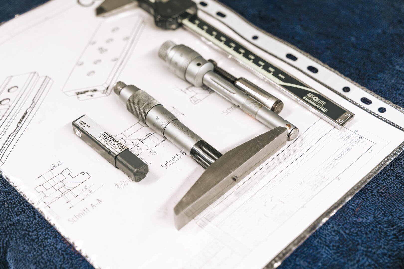 A series of precision measuring tools, including a micrometer and calipers, are placed on technical drawings with a blue background.