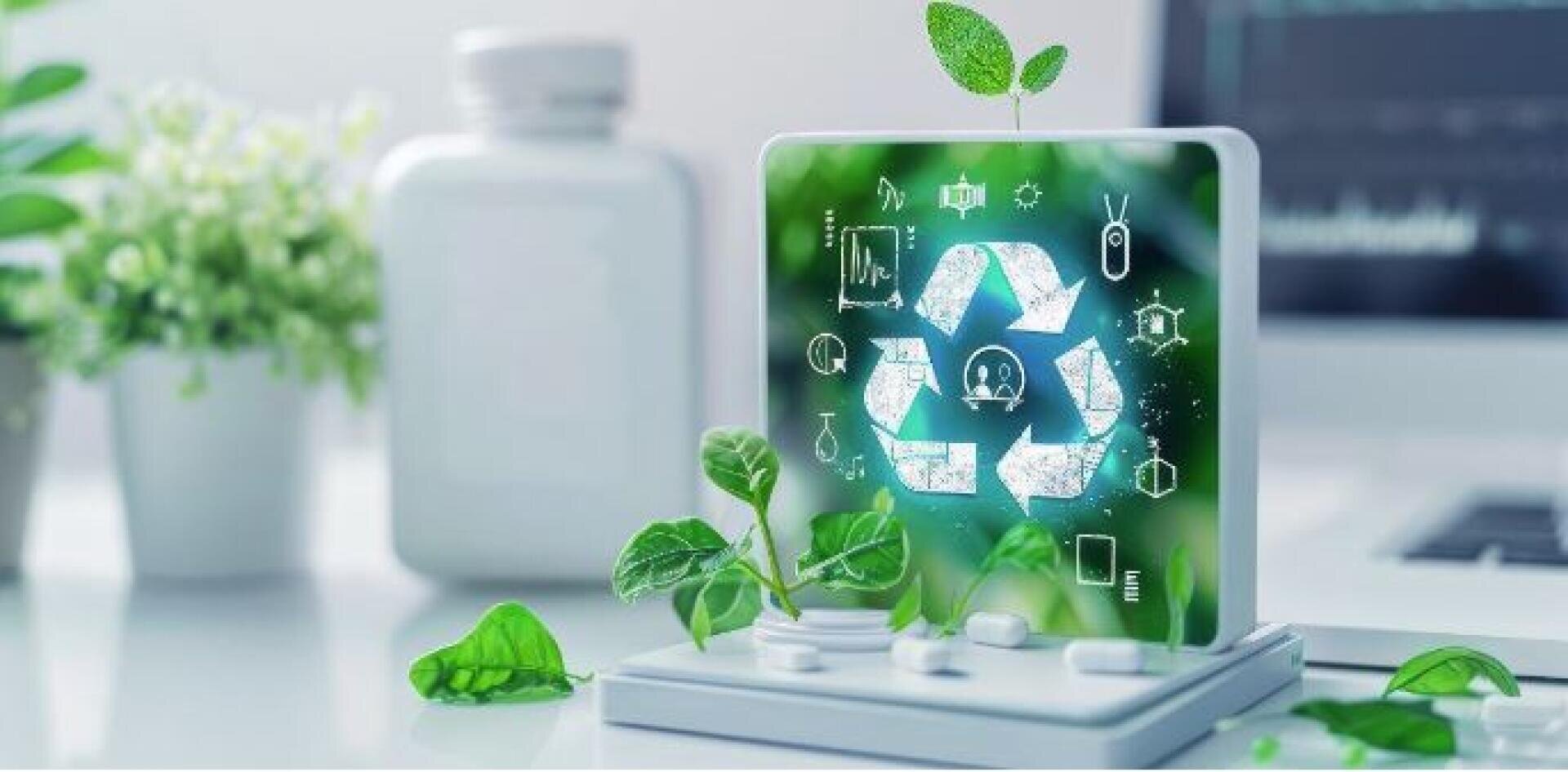 A digital tablet displays a glowing recycling symbol surrounded by eco-related icons. Green leaves and small plants grow around the device, symbolizing sustainability and environmental technology. A blurred office setting is in the background.