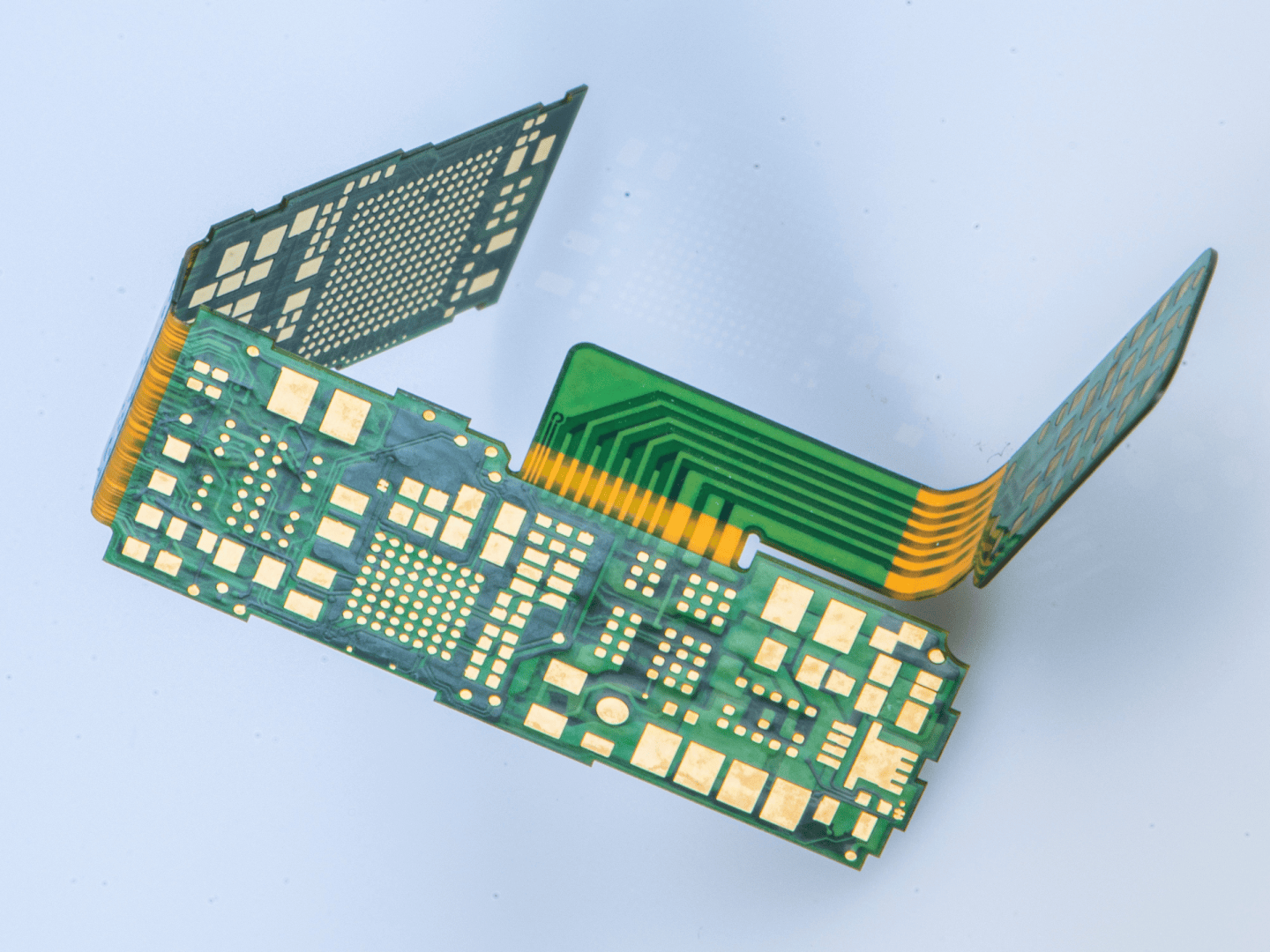 A green and yellow flexible printed circuit board with multiple sections and gold contact pads is bent at several angles, showcasing its adaptability and intricate design.
