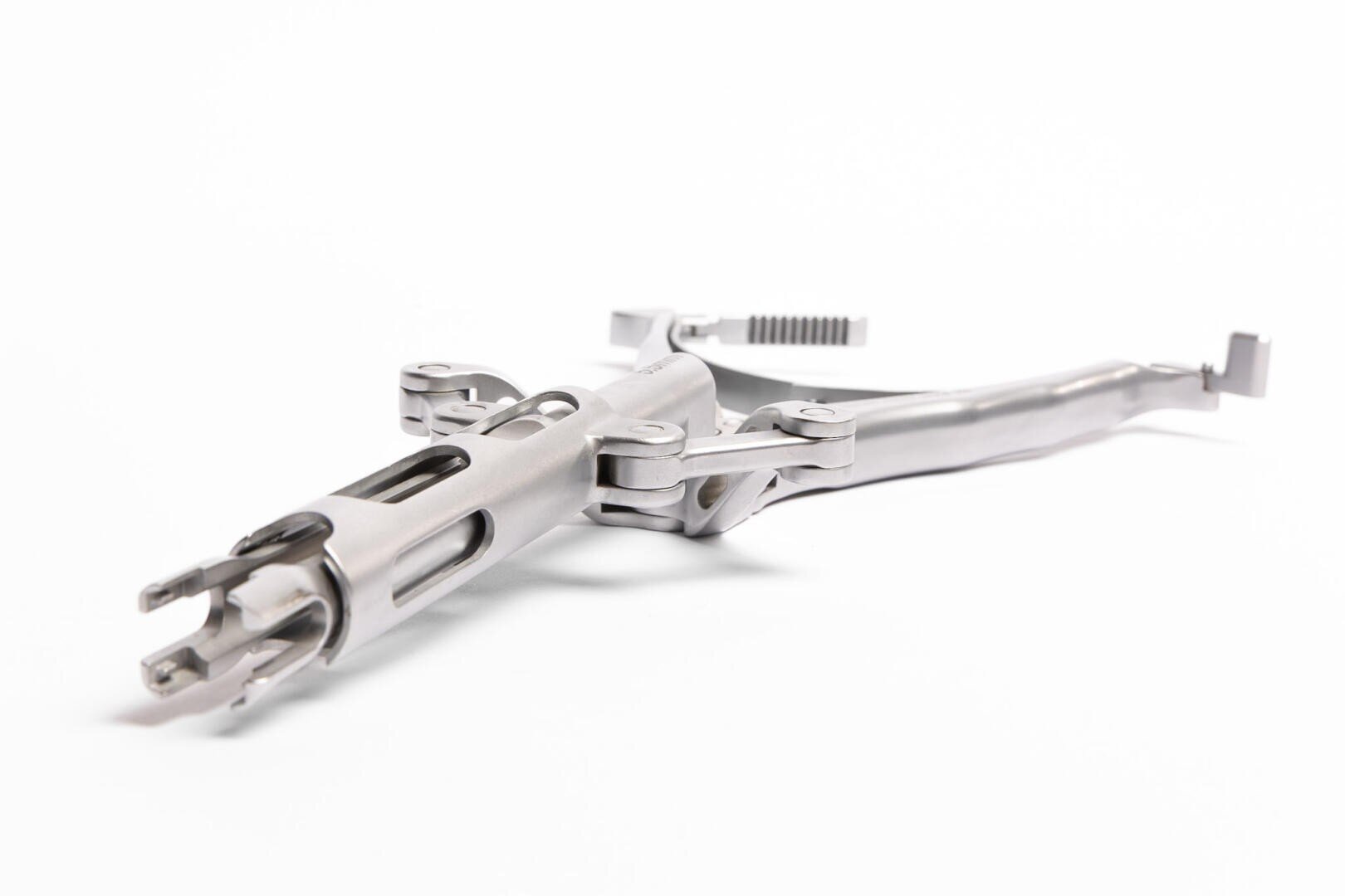 A metallic surgical instrument with multiple hinged parts and precision joints, photographed against a white background. The tool features openings and adjustable sections that give it a complex, mechanical appearance.