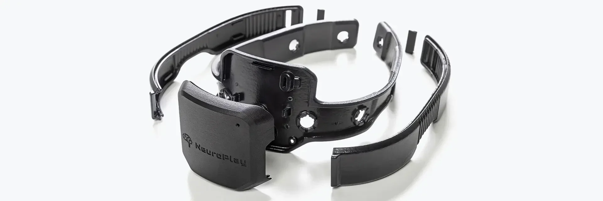 A black Neuroplay-branded headband device with multiple detachable segments and ports, designed for wearing around the head.