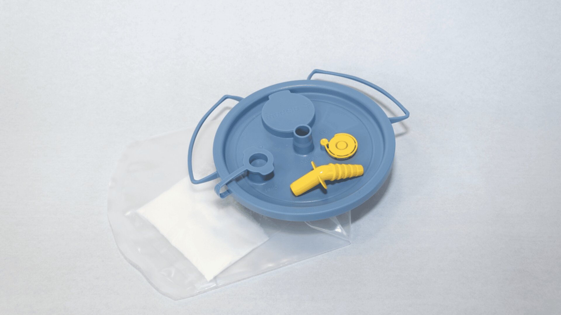 Ein blauer Kunststoffdeckel mit Griffen und gelben Ventilelementen ist an einem transparenten Beutel mit weißem Einsatz auf hellem Hintergrund angebracht.