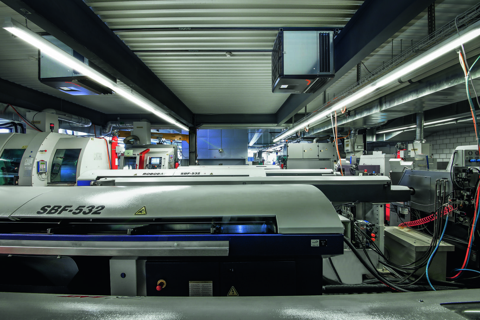 Eine moderne Industriehalle mit großen automatisierten CNC-Maschinen, darunter eine mit der Bezeichnung SBF-532, umgeben von Metallteilen, Kabeln und Deckenbeleuchtung in einem gut organisierten, sauberen Raum.