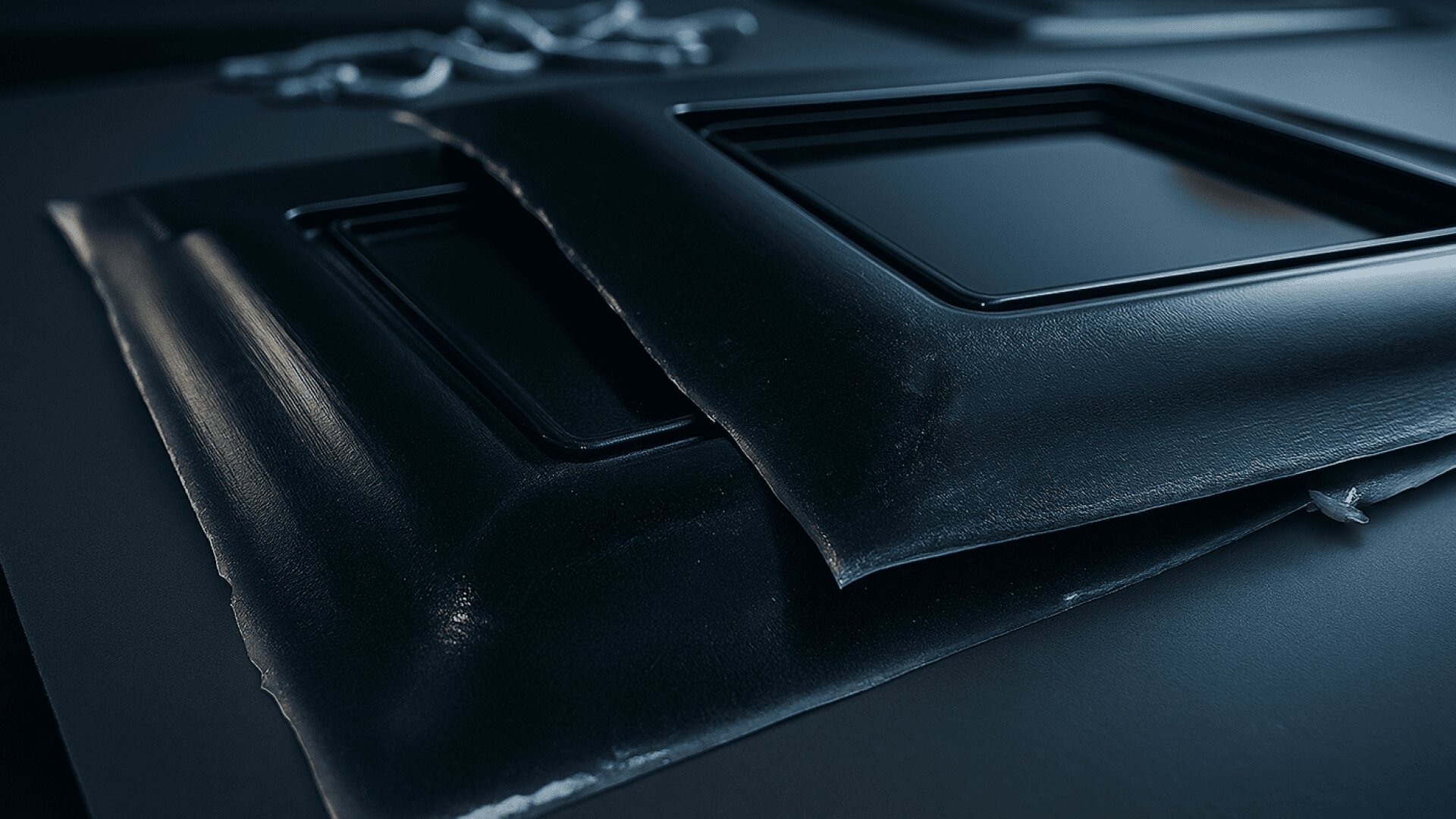 Nahaufnahme von schwarzen, glänzenden rechteckigen Platten, die möglicherweise in einer Fertigungs- oder Industrieumgebung geformt oder gepresst werden, mit glatten Texturen und definierten Kanten auf einer dunklen Oberfläche.
