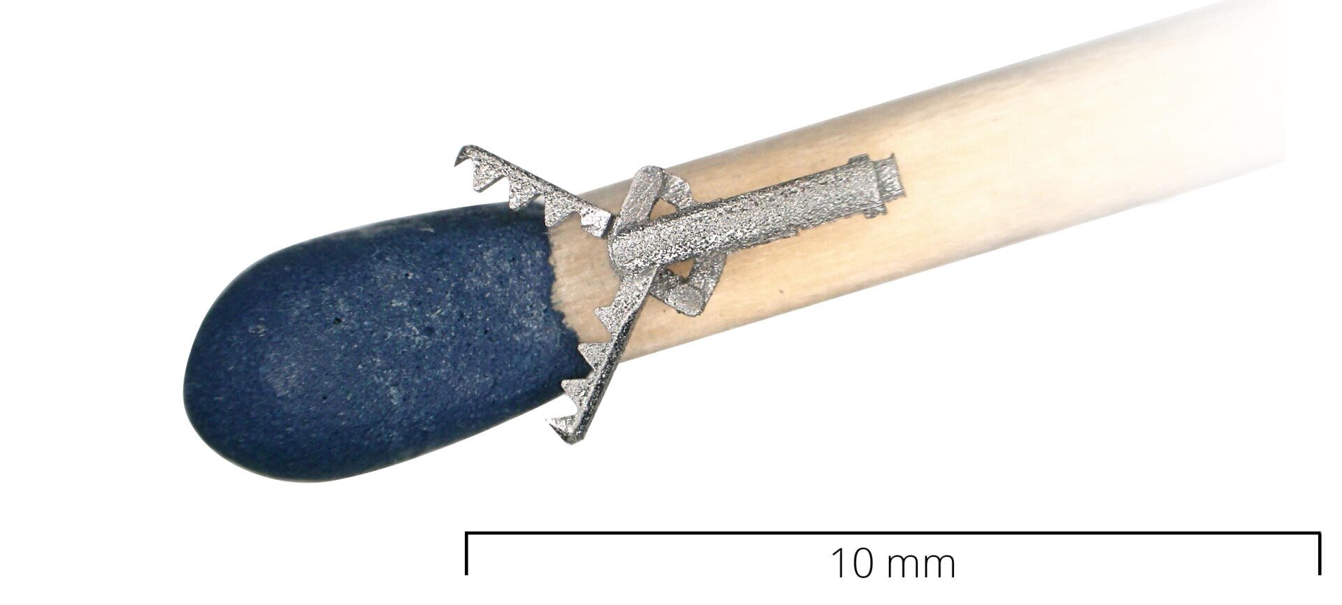 Ein winziges medizinisches Metallgerät mit gezackten Rändern ist an der Spitze eines Streichholzes befestigt, das als Maßstab dient. Unter dem Streichholz befindet sich ein 10-mm-Skalierungsbalken, der die geringe Größe des Geräts verdeutlicht.