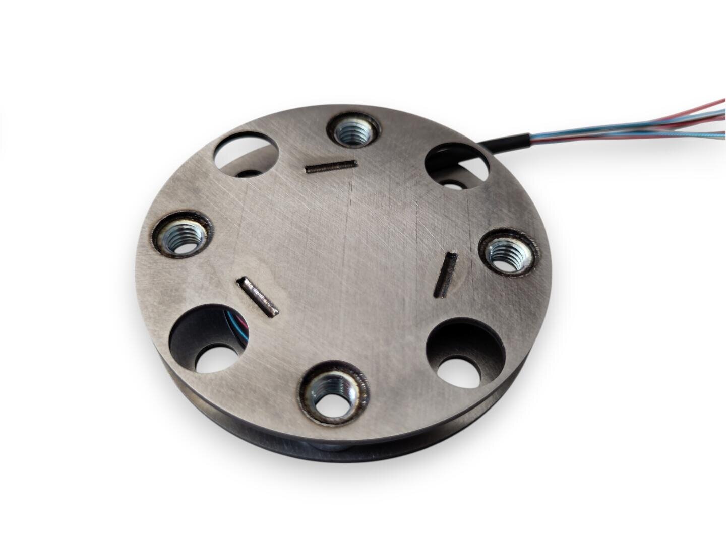 A round load cell sensor made of metal with four large holes, two small slots and several thin wires on the side, insulated on a white background.