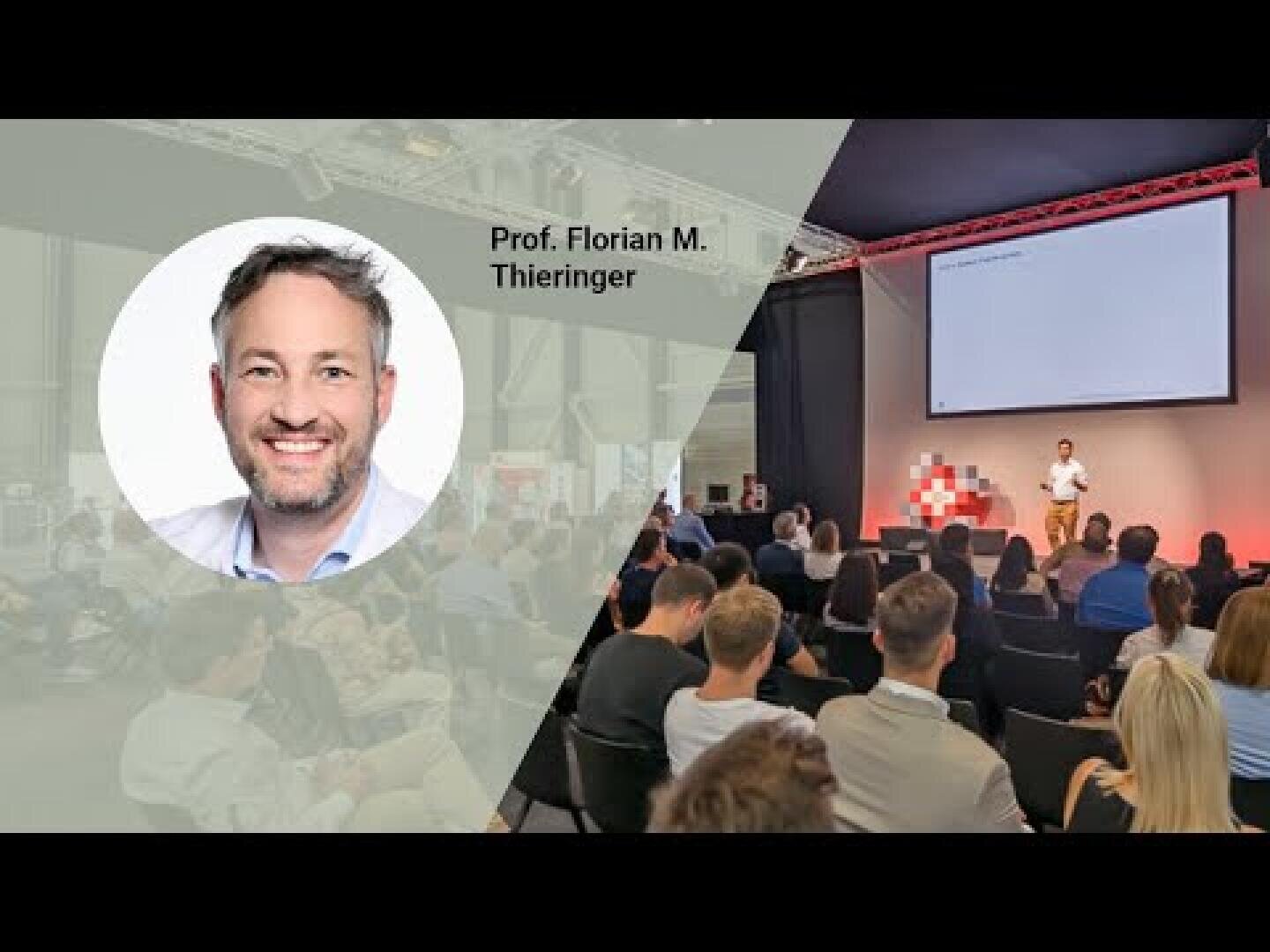 A large audience listens to a speaker presenting on stage with a projection screen. An insert shows a portrait of Prof. Florian M. Thieringer and his name. The backdrop is modern and professionally lit.