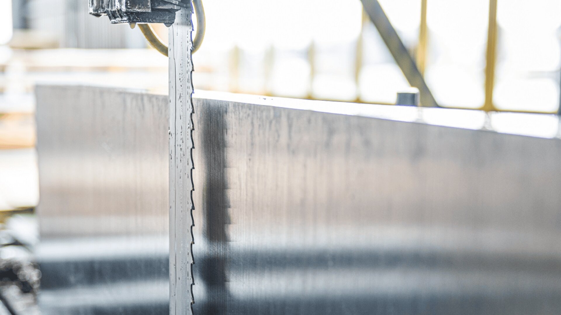 Nahaufnahme einer horizontalen Bandsäge, die eine dicke Metallplatte in einer Werkstatt durchschneidet, mit sichtbaren Metallspänen und unscharfem industriellen Hintergrund.