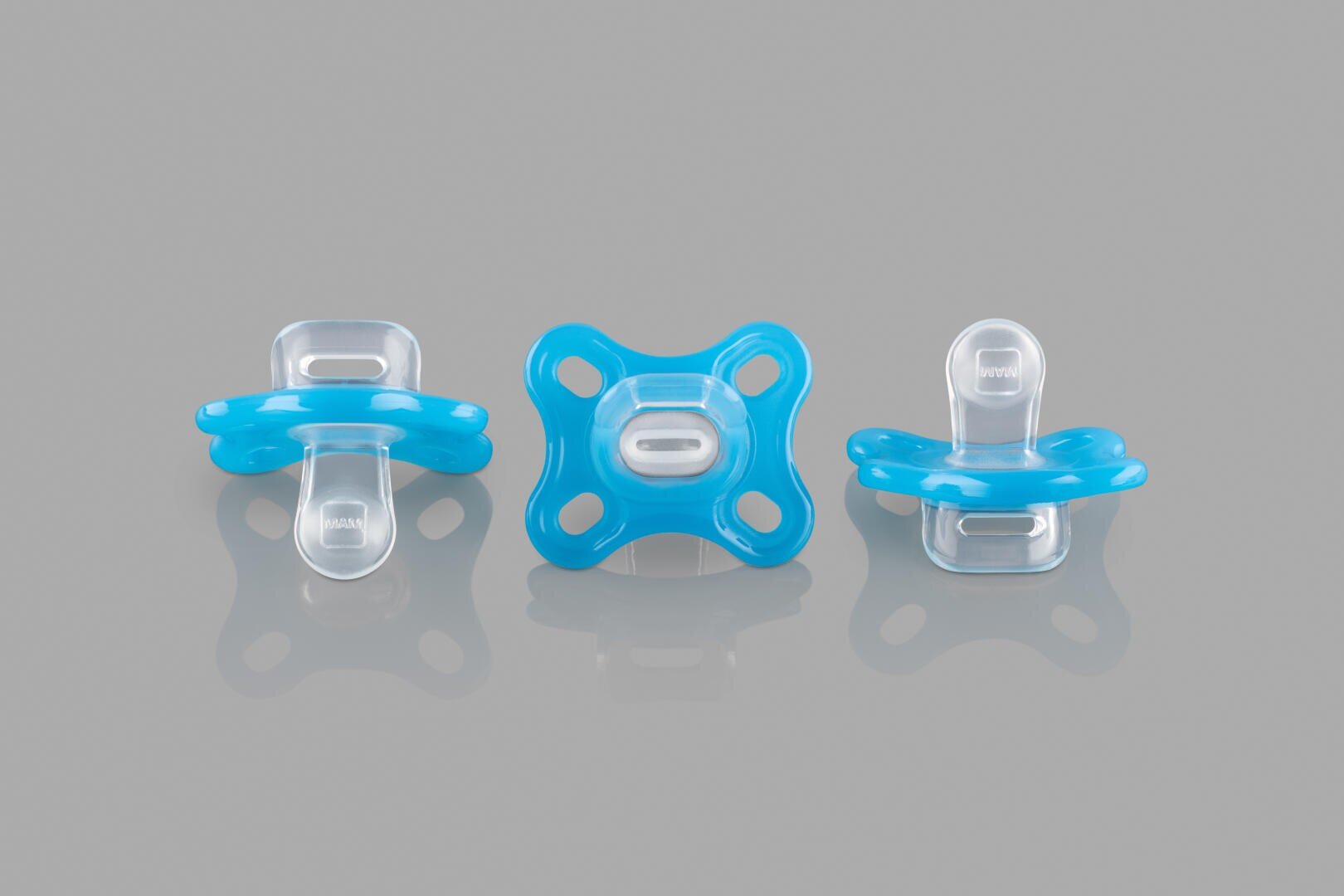 On a gray surface, three blue and transparent baby pacifiers are shown in front, side and back views.
