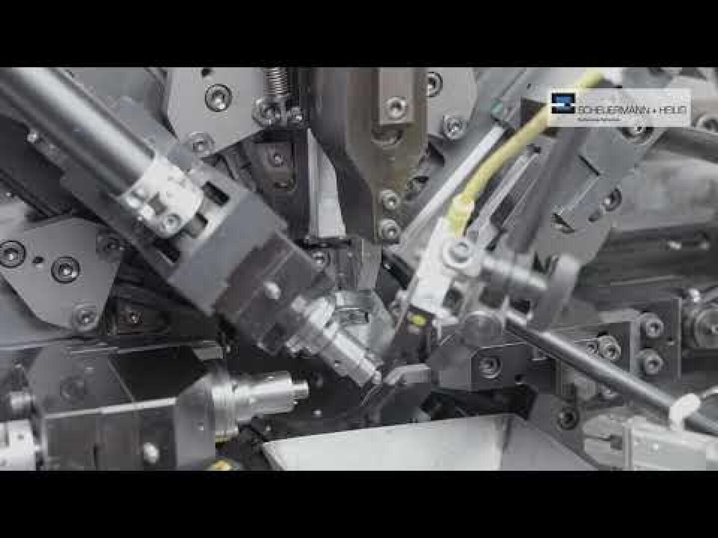 Nahaufnahme einer Industriemaschine mit mehreren Metallteilen, Roboterarmen und Rohren in Betrieb; das Logo Schleiferei + Heilig erscheint in der oberen rechten Ecke.