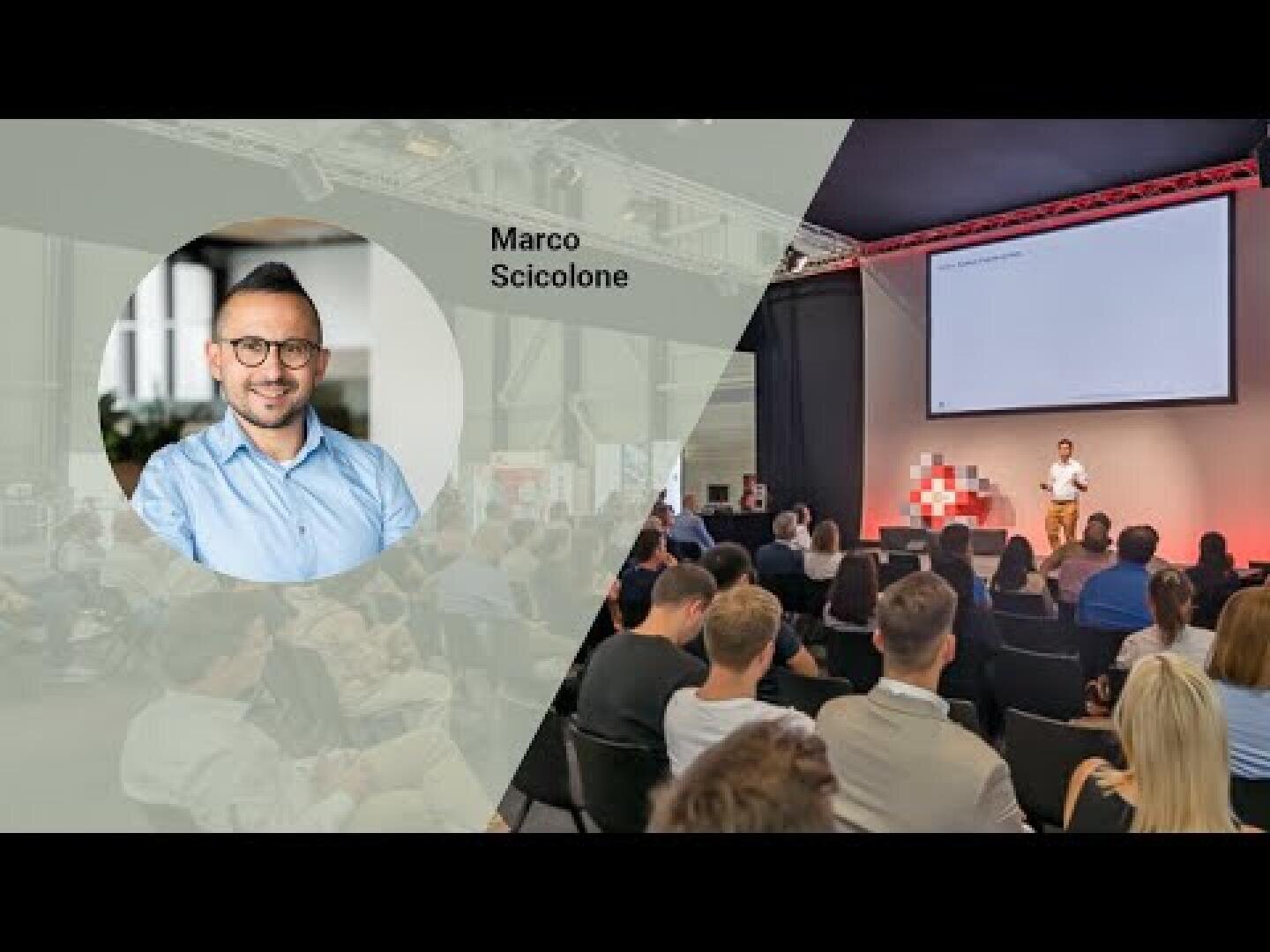 Ein Mann hält eine Präsentation auf der Bühne vor einem Publikum in einem modernen Veranstaltungsraum. Die linke Seite zeigt ein eingefügtes Kopfbild eines lächelnden Mannes mit der Aufschrift Marco Scicolone. Auf einem großen Bildschirm wird ein Dia hinter dem Redner angezeigt.