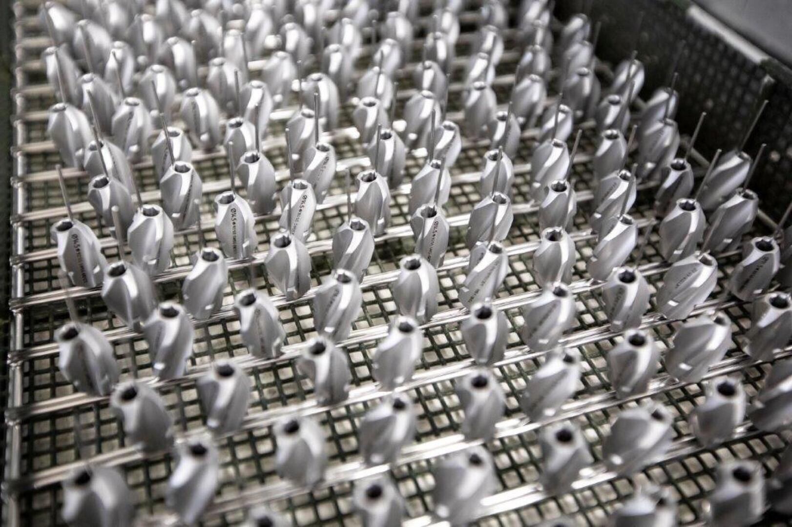 Reihen identischer Metallteile sind ordentlich auf einem Metallgitter angeordnet, wahrscheinlich in einer Fabrik oder Fertigungsanlage, was den Eindruck von Gleichförmigkeit und technischer Präzision vermittelt.