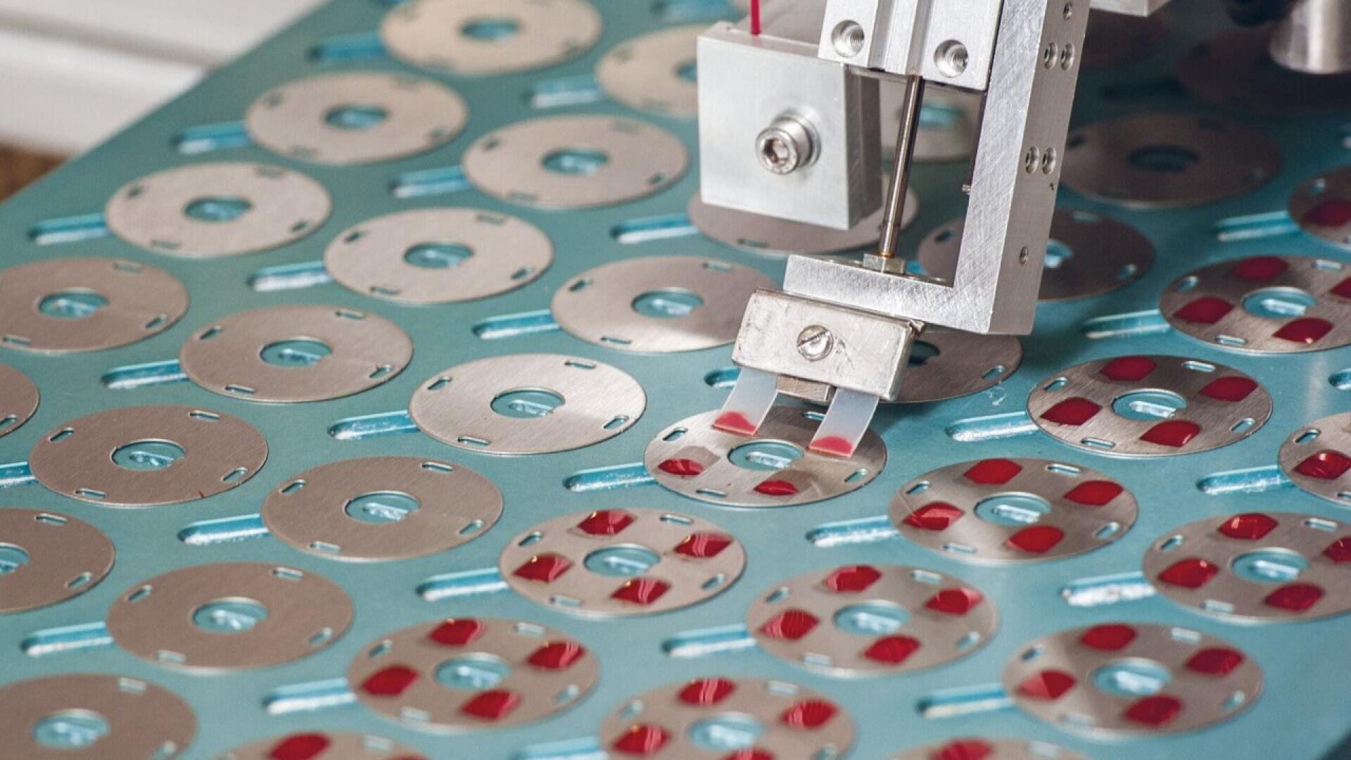 A robotic arm assembles or inspects circular metal components with holes, arranged in rows on a blue surface.