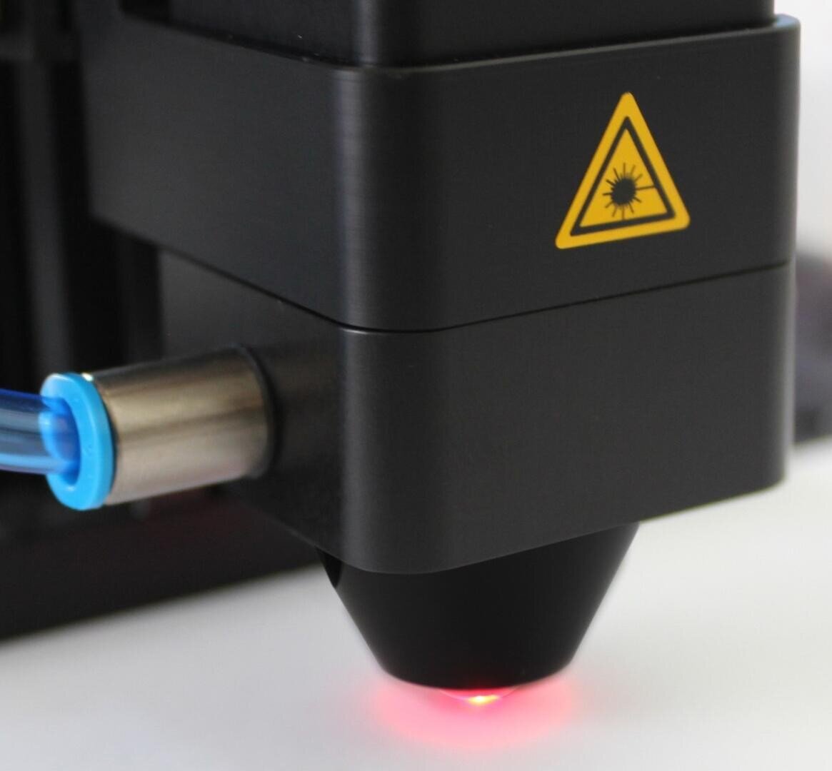 Nahaufnahme eines schwarzen Lasergeräts mit einem rot leuchtenden Licht an der Spitze und einem gelben Laserwarnsymbol an der Seite. An der linken Seite ist ein blau gekapseltes Metallteil angebracht.