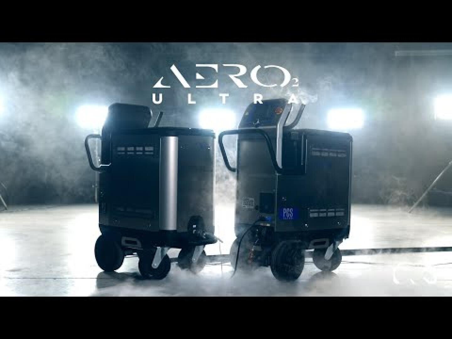 Two sleek, black industrial machines labeled AERO2 ULTRA stand side by side on a misty floor, illuminated by bright lights in the background, creating a dramatic atmosphere.