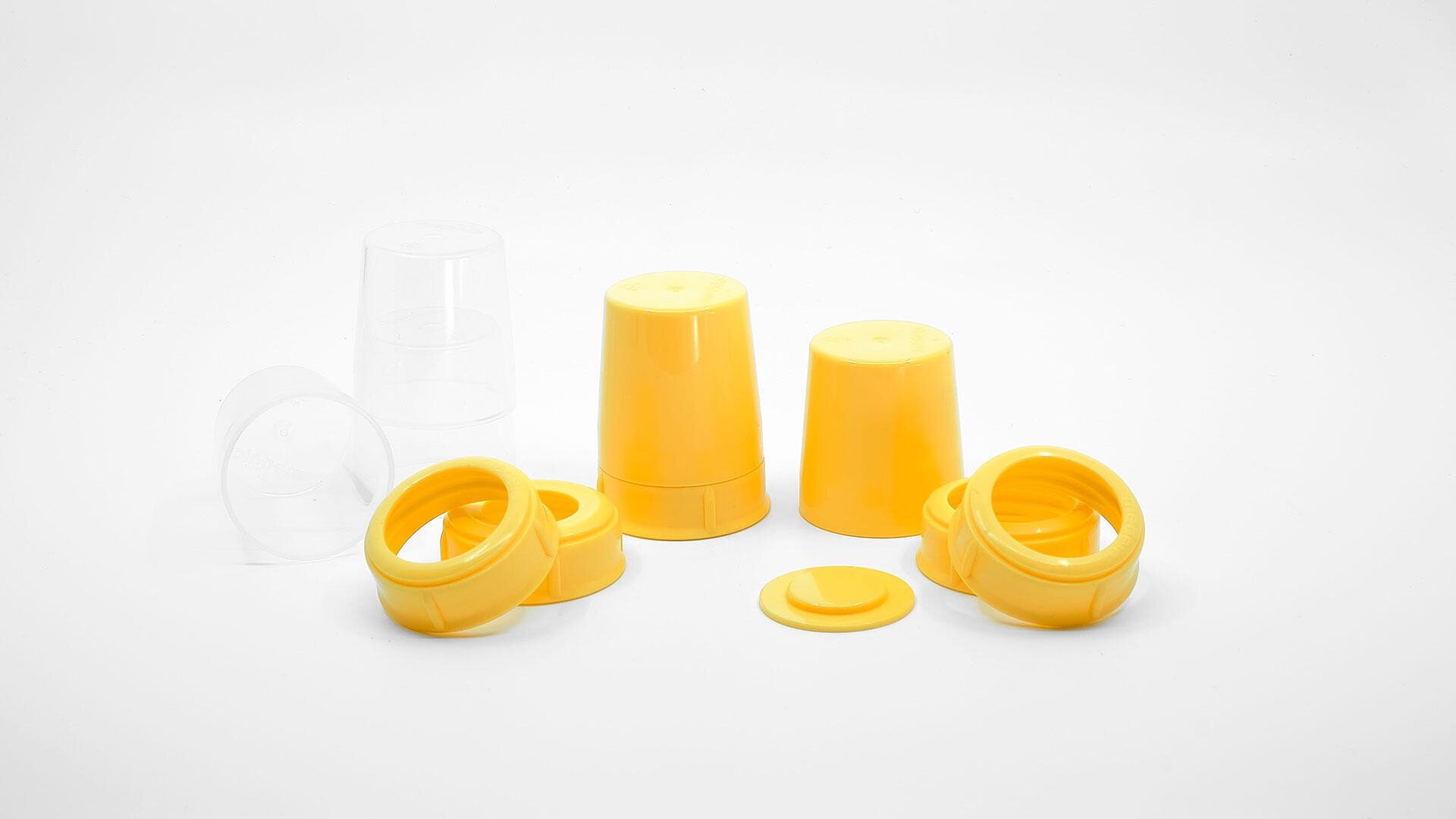 Eine Gruppe gelber Plastikbecher und -ringe, einige stehen aufrecht, andere sind umgekippt, mit einem durchsichtigen Plastikbecher im Hintergrund, alles auf einer weißen Oberfläche.