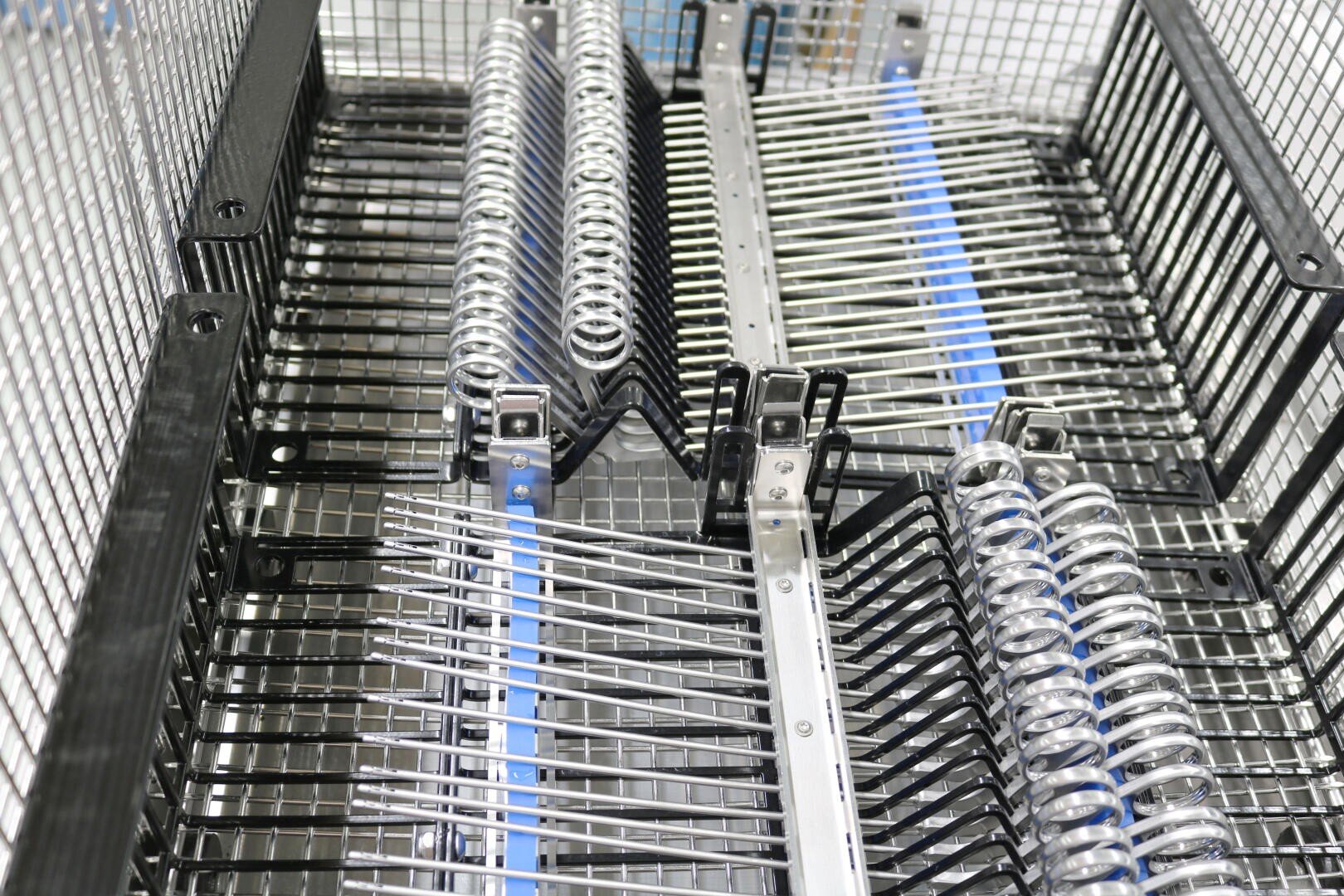 Close-up of a metal wire basket containing orderly surgical instruments and tools, including rows of metal rods and spring-like components, all neatly arranged for sterilization.