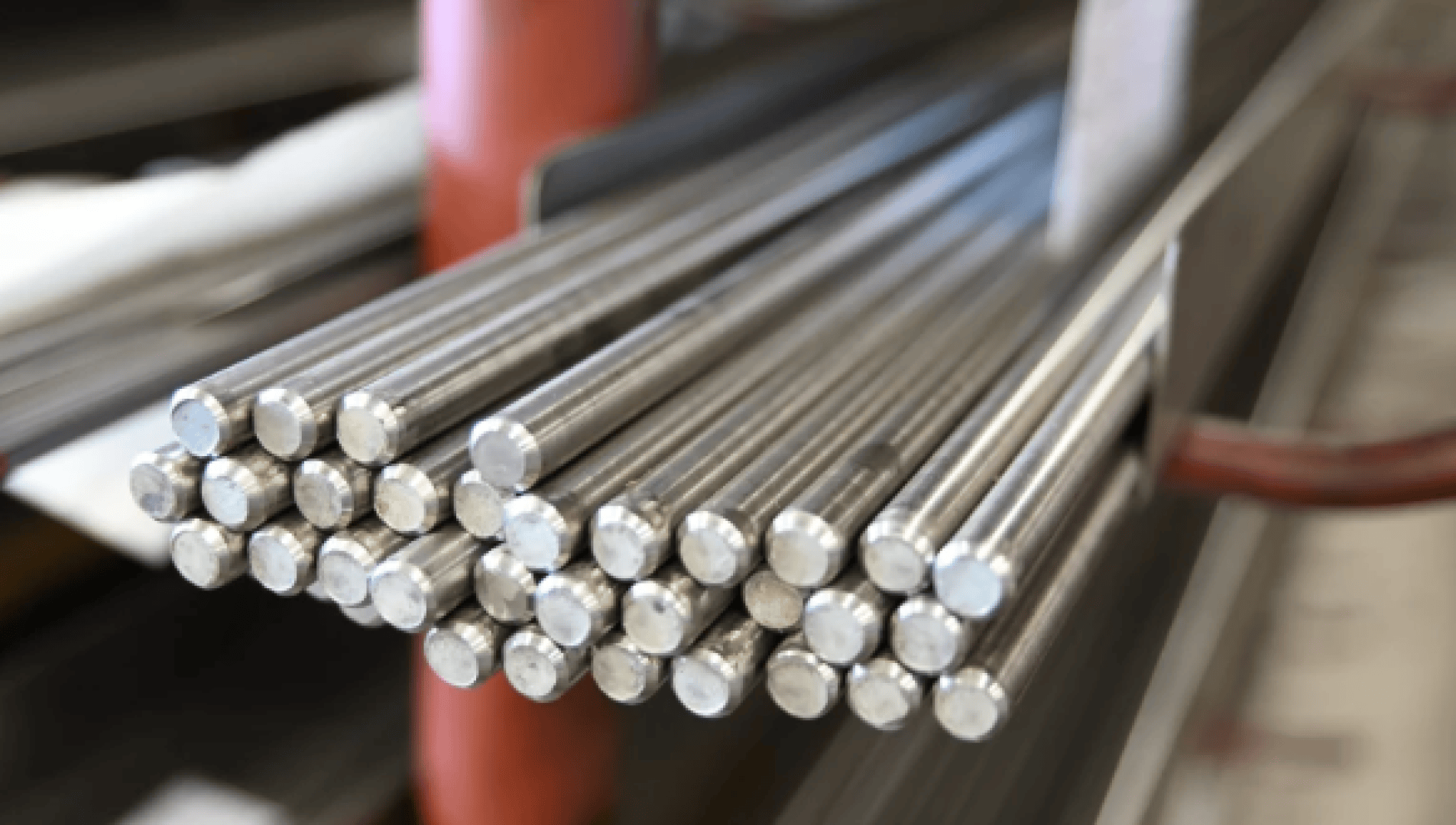 Nahaufnahme von gebündelten Metallstäben mit glatten, runden Enden, die auf einem Metallgestell in einer scheinbar industriellen Umgebung gestapelt sind.