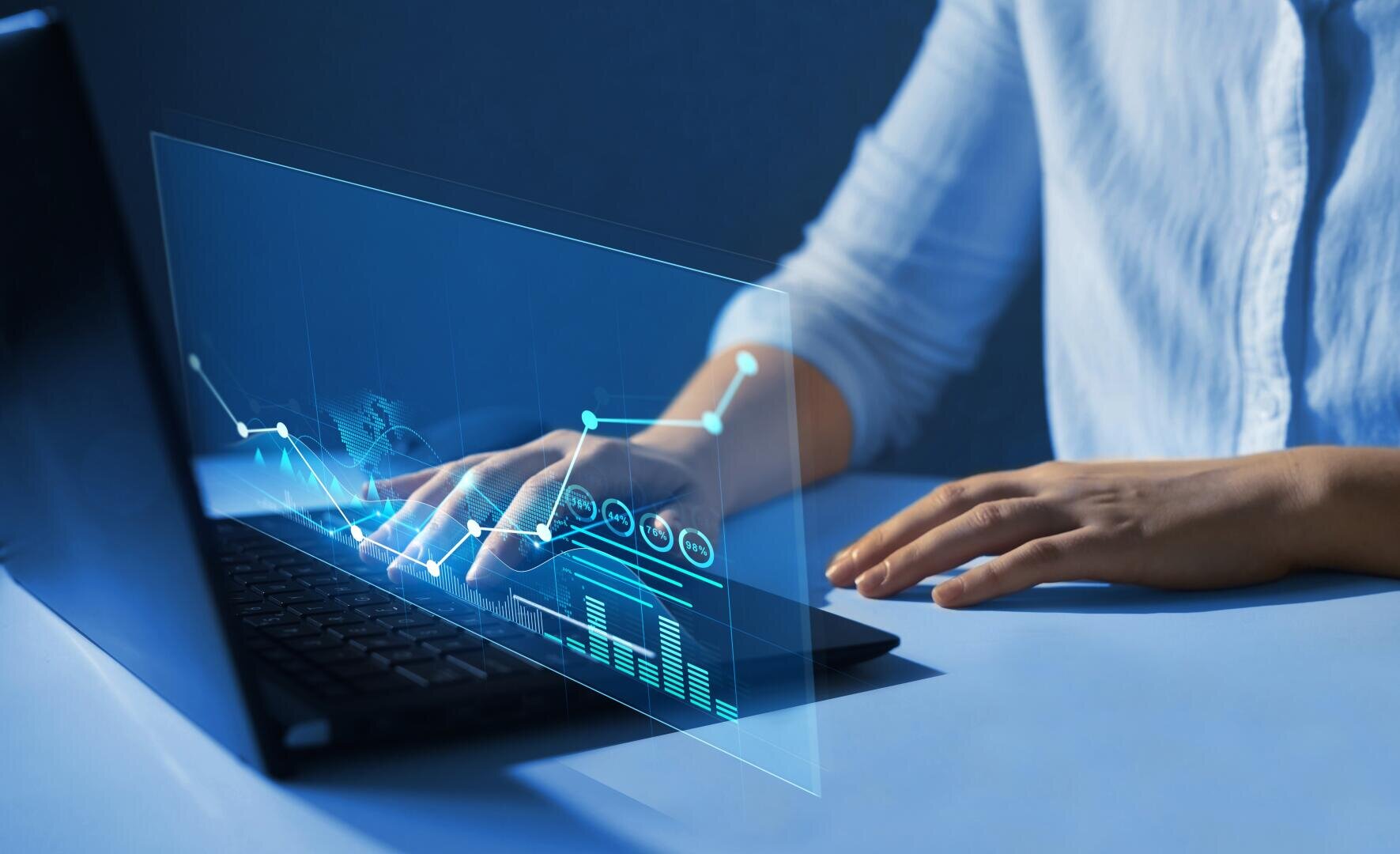 A person using a laptop with a virtual screen that displays data charts and graphs depicting digital analysis or financial technology on a blue background.