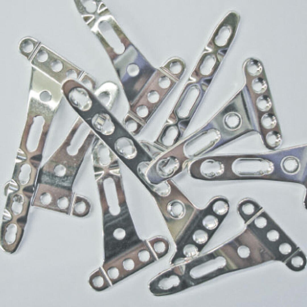 Ein verstreuter Stapel glänzender orthopädischer Knochenplatten aus Metall, jede mit mehreren runden und ovalen Löchern für chirurgische Schrauben, dargestellt auf einem schlichten hellen Hintergrund.