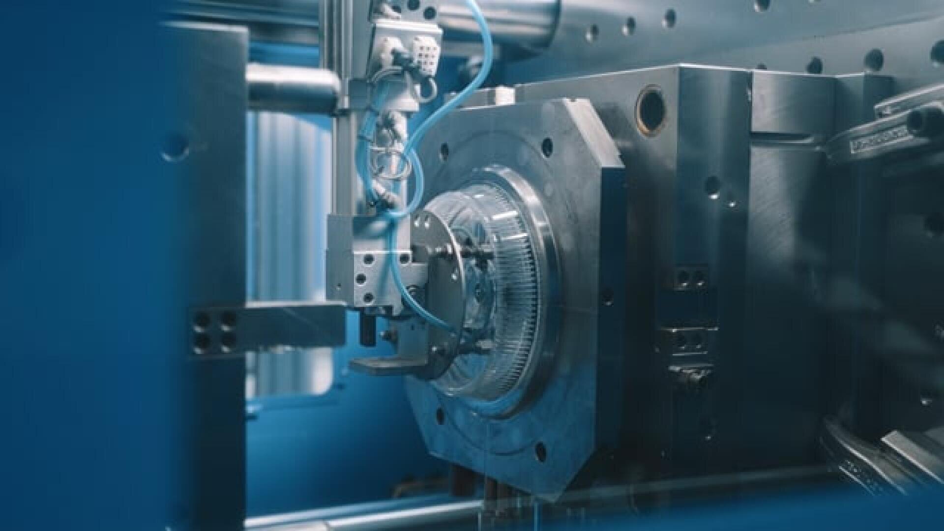 Close-up of an industrial robotic arm operating a metal part in a machine, probably in a manufacturing or assembly process, with blue lighting and a precise high-tech environment.