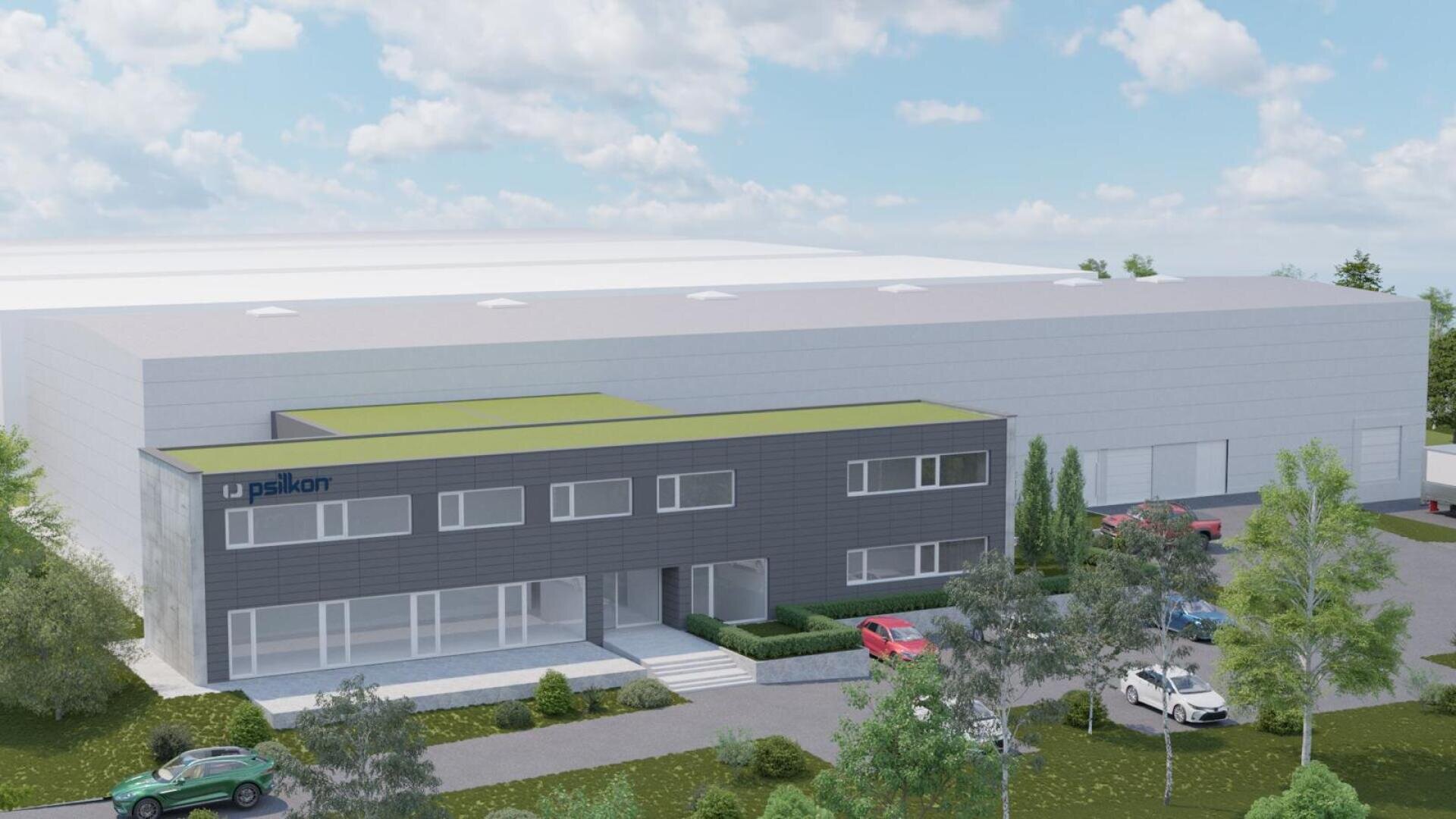 A modern industrial building complex with a gray facade, green rooftop, and large windows. Several cars are parked nearby, and trees and shrubs surround the property under a partly cloudy sky.