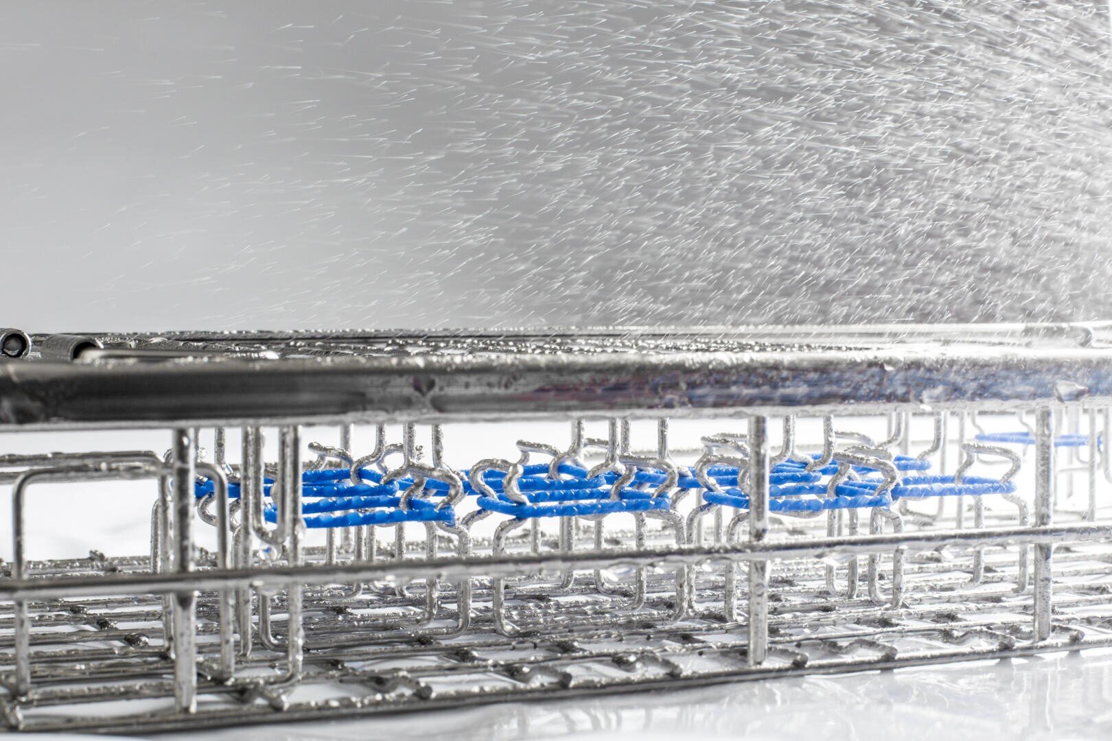 Close-up of the inside of a dishwasher, showing water spraying over metal racks with blue plastic accents, highlighting the water cleaning process.
