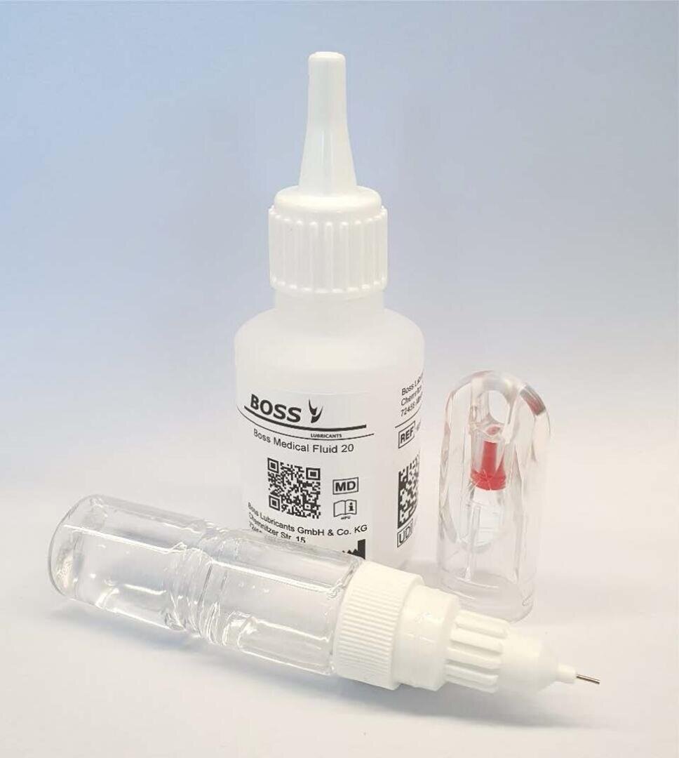 Three medical items: a white pressurized bottle labeled BOSS Medical Fluid 20, a clear vial with a white tip and a small clear cap with a red insert, all on a plain white surface.