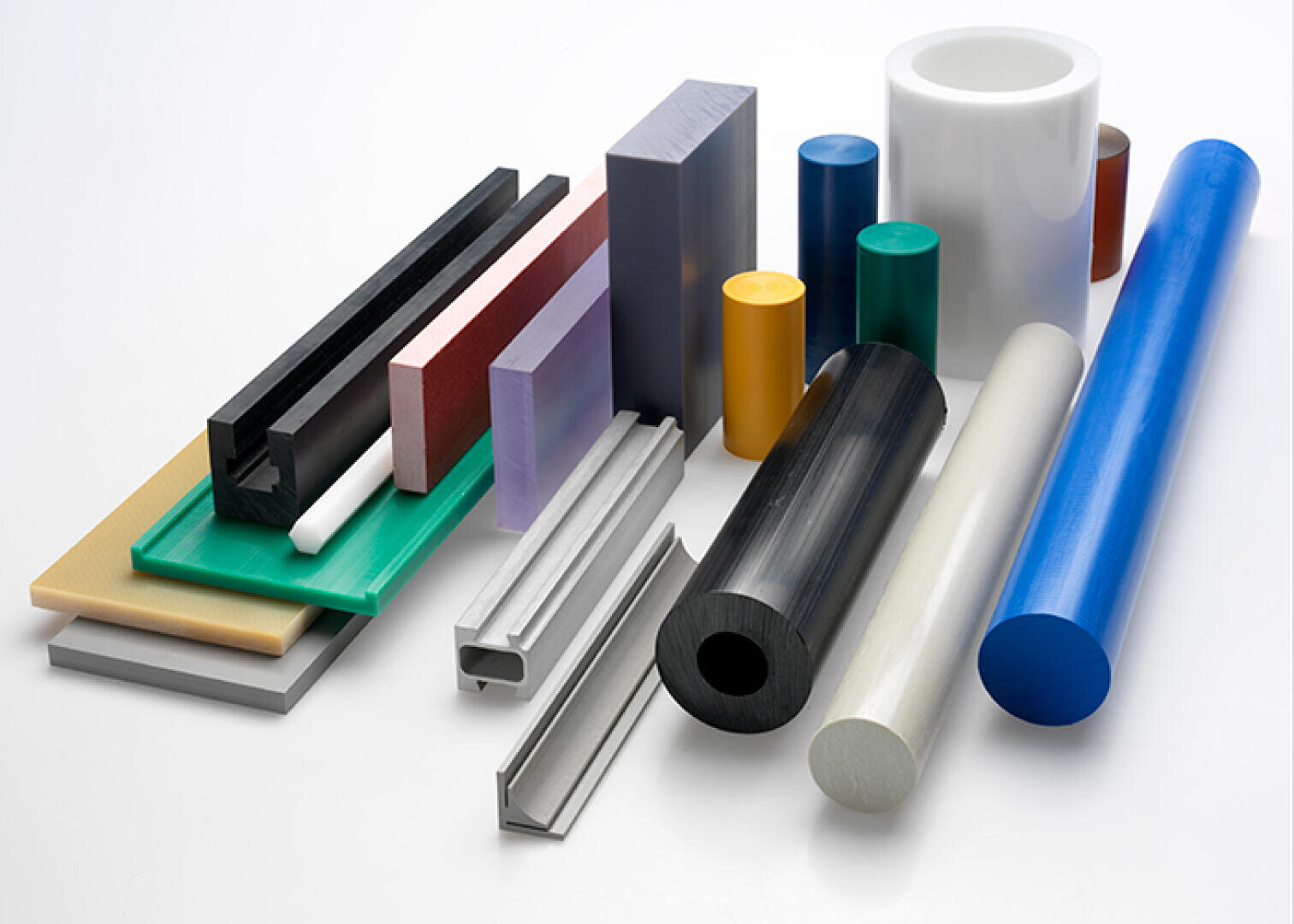 Eine Vielzahl von bunten Kunststoffstäben, -platten und -stangen in verschiedenen Formen und Größen sind auf einer weißen Fläche angeordnet. Zu den Gegenständen gehören Zylinder, Rechtecke und U-Kanäle in verschiedenen Farben.