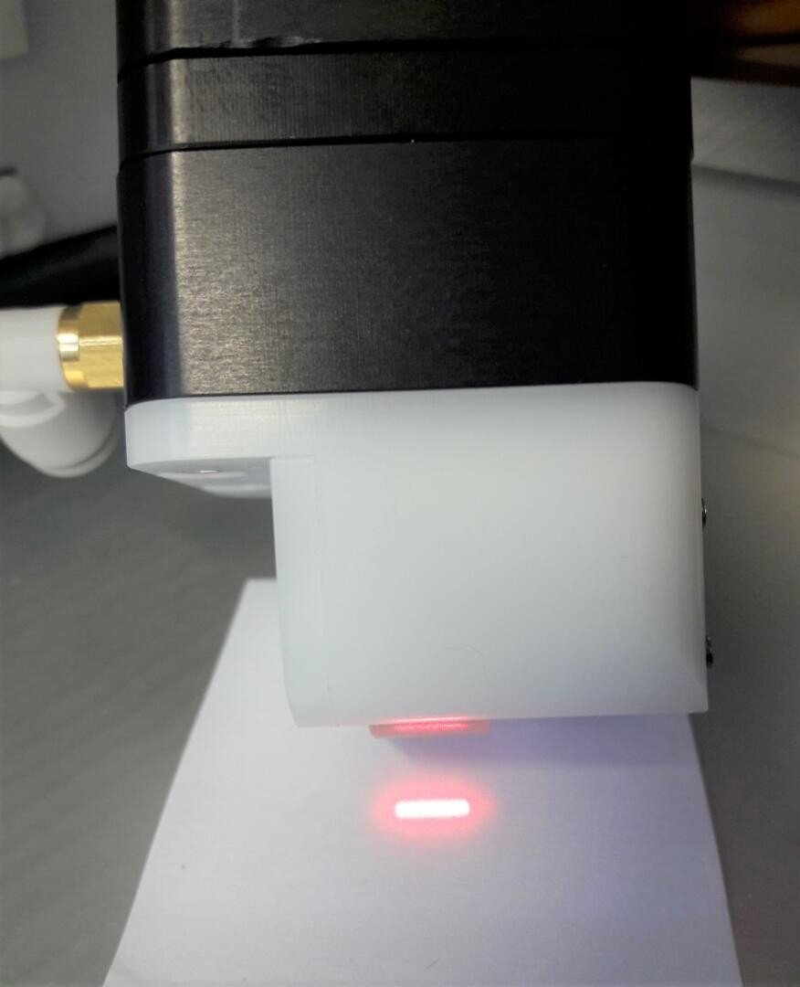 Nahaufnahme eines schwarz-weißen elektronischen Geräts, das ein kleines rotes Laserrechteck auf ein weißes Blatt Papier projiziert.
