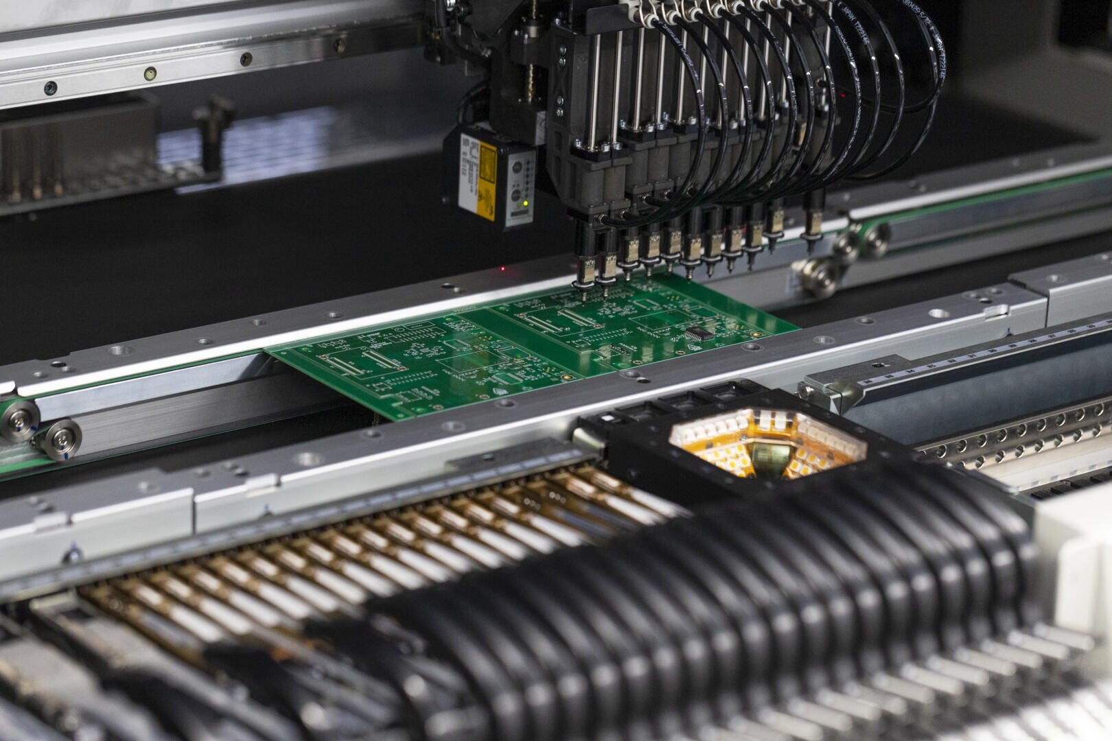 Close-up of a machine that places components on green circuit boards during an automated electronics manufacturing process.