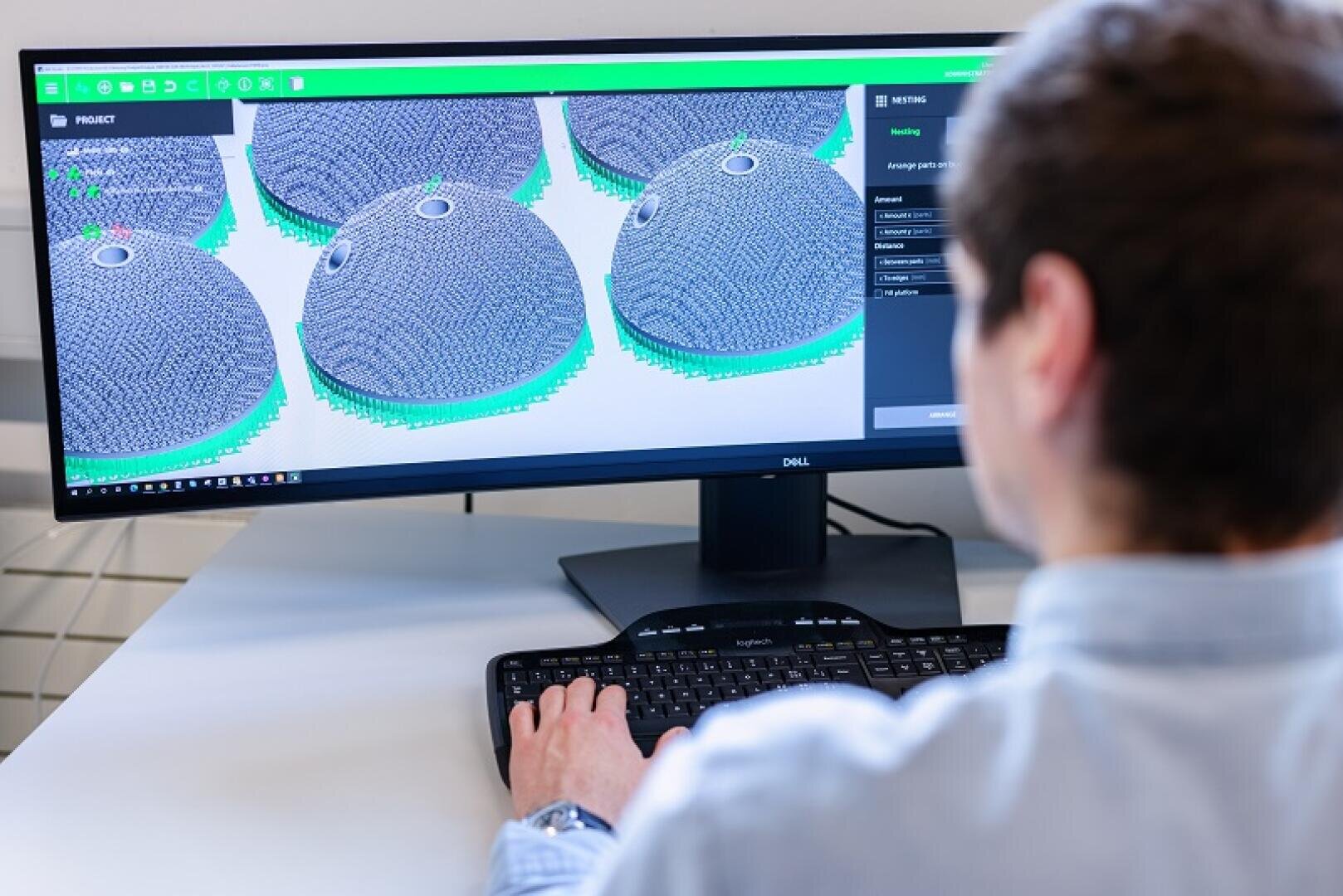 A person uses a computer to display 3D models of hemispherical objects with mesh patterns on a large monitor, probably working with design or engineering software.