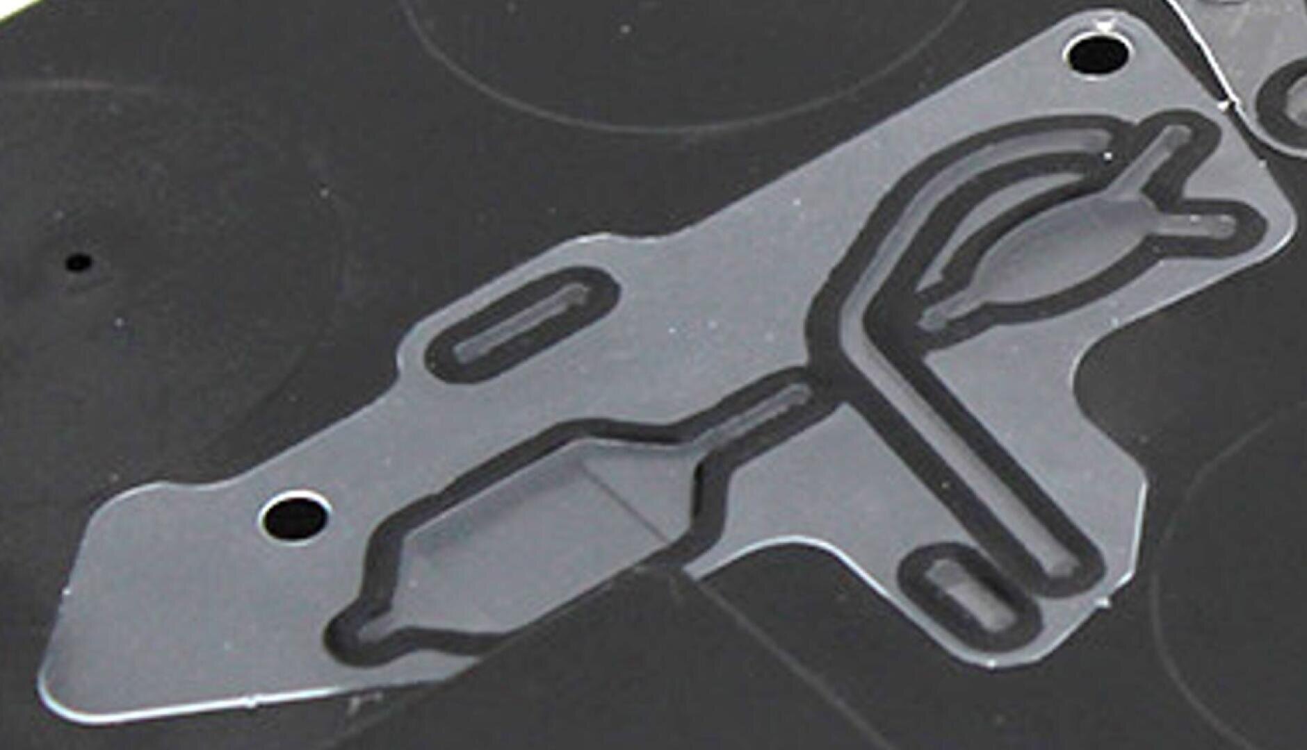 Nahaufnahme eines schwarzen Mikrofluidchips aus Kunststoff mit transparenten Kanälen und zwei runden Löchern, die komplizierte Pfade zeigen, die für die Bewegung und Analyse von Flüssigkeiten ausgelegt sind.