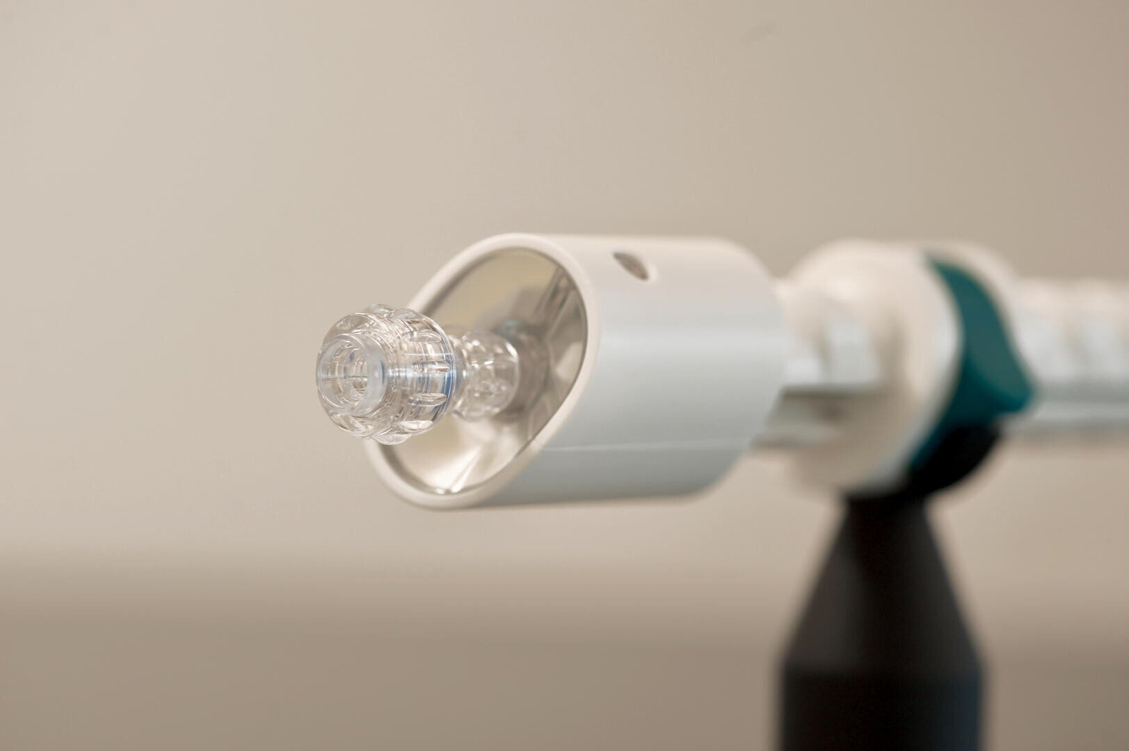 Close-up of a medical device with a transparent plastic tip and a white and teal body, set against a neutral, blurred background.