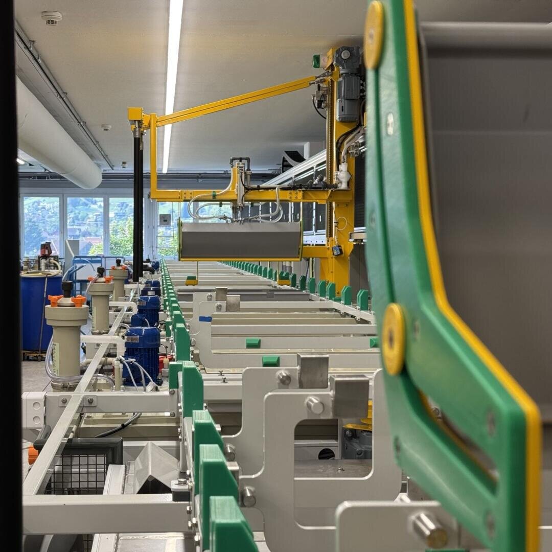 Eine Nahaufnahme einer automatisierten industriellen Fertigungsstraße mit grünen und gelben Komponenten in einer hell erleuchteten Fabrik, in der Maschinen und Geräte in parallelen Reihen angeordnet sind.