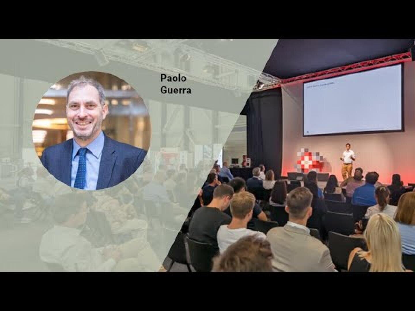 Ein Geschäftsmann, Paolo Guerra, wird links hervorgehoben, während rechts ein Redner in einem modernen Konferenzraum mit Großbildschirm vor einem Publikum spricht.