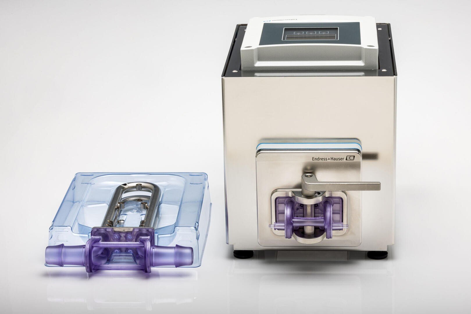 Ein Labor- oder Industriegerät aus rostfreiem Stahl mit digitaler Anzeige und der Aufschrift Endress+Hauser steht neben einem abnehmbaren Bauteil mit durchscheinenden blauen und violetten Kunststoffteilen.