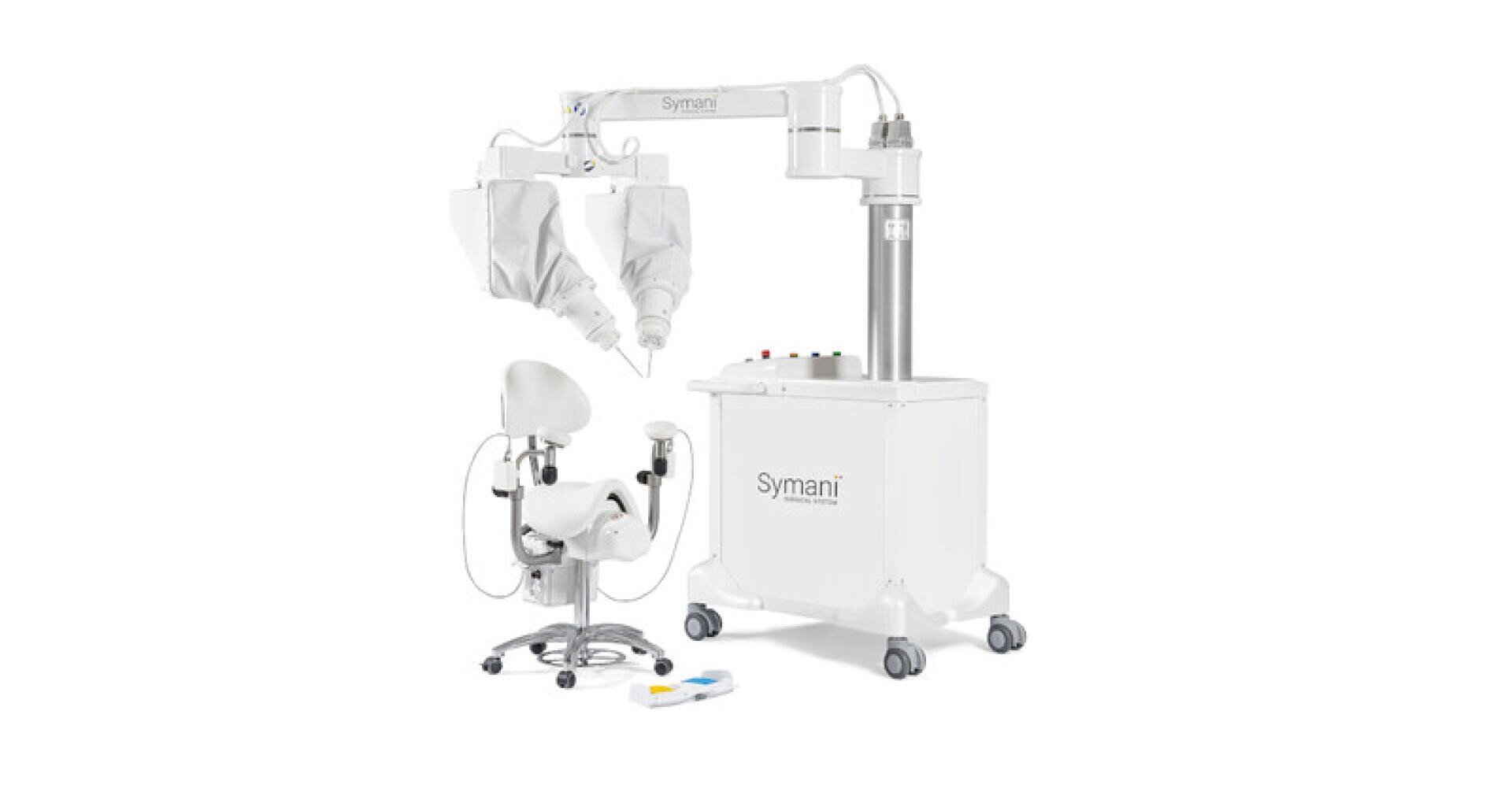 A modern medical robotic system with an adjustable chair, two robotic arms covered with white cloths, a control panel and the Symani brand name on the base, all against a white background.