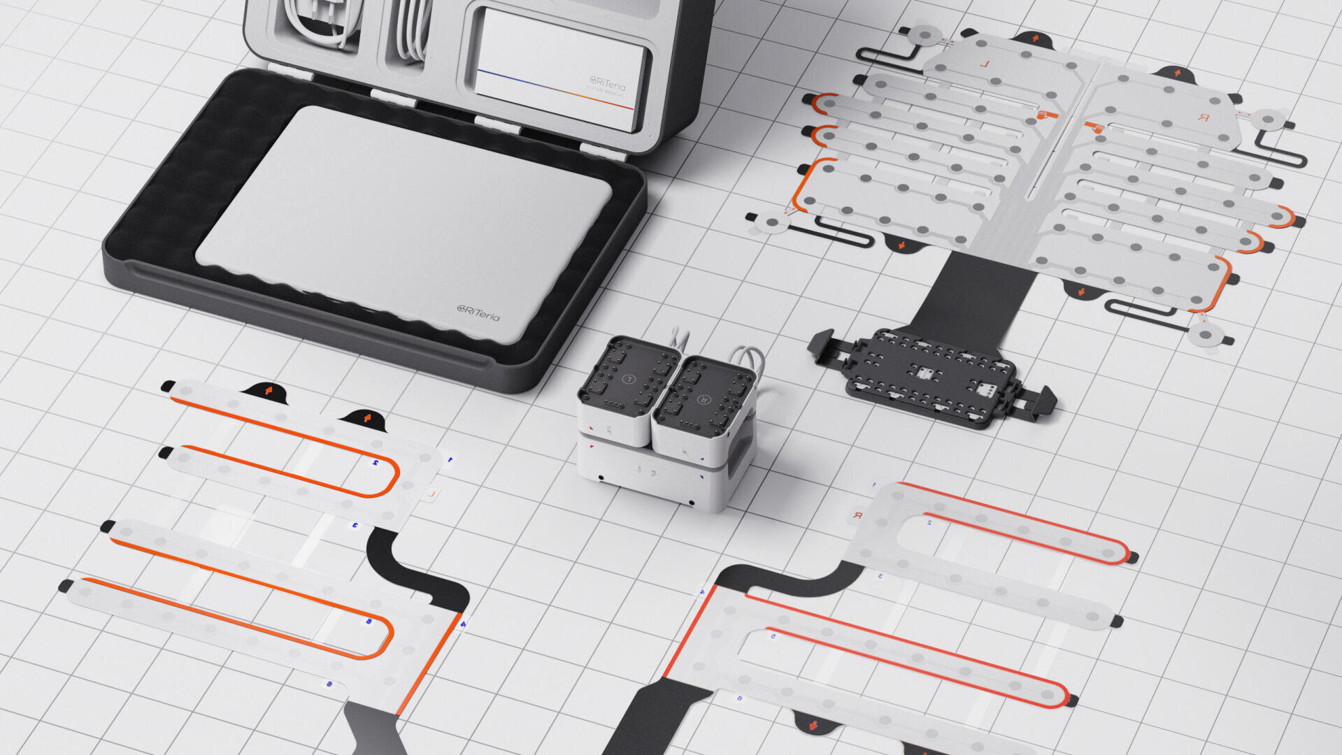 A modern modular electronic kit is arranged on a grid surface, including a sleek silver housing, cables, circuit boards with orange and black traces and two connected black and white units in the center.