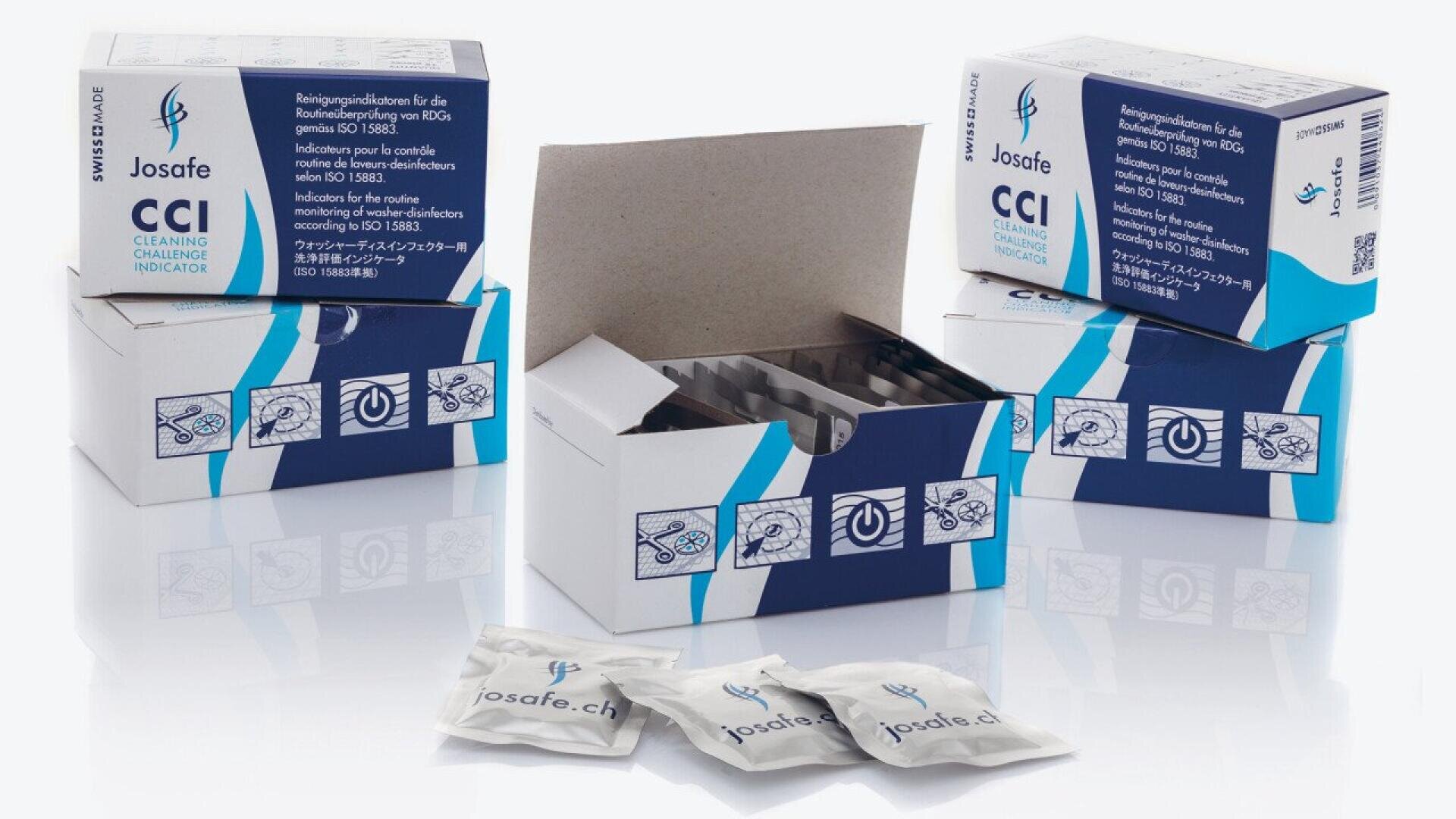 Three blue and white boxes labeled Josafe CCI Cleaning Challenge Indicator are displayed, with one open showing dividers inside. Three small sealed pouches lie in the foreground. Text and icons decorate the packaging.