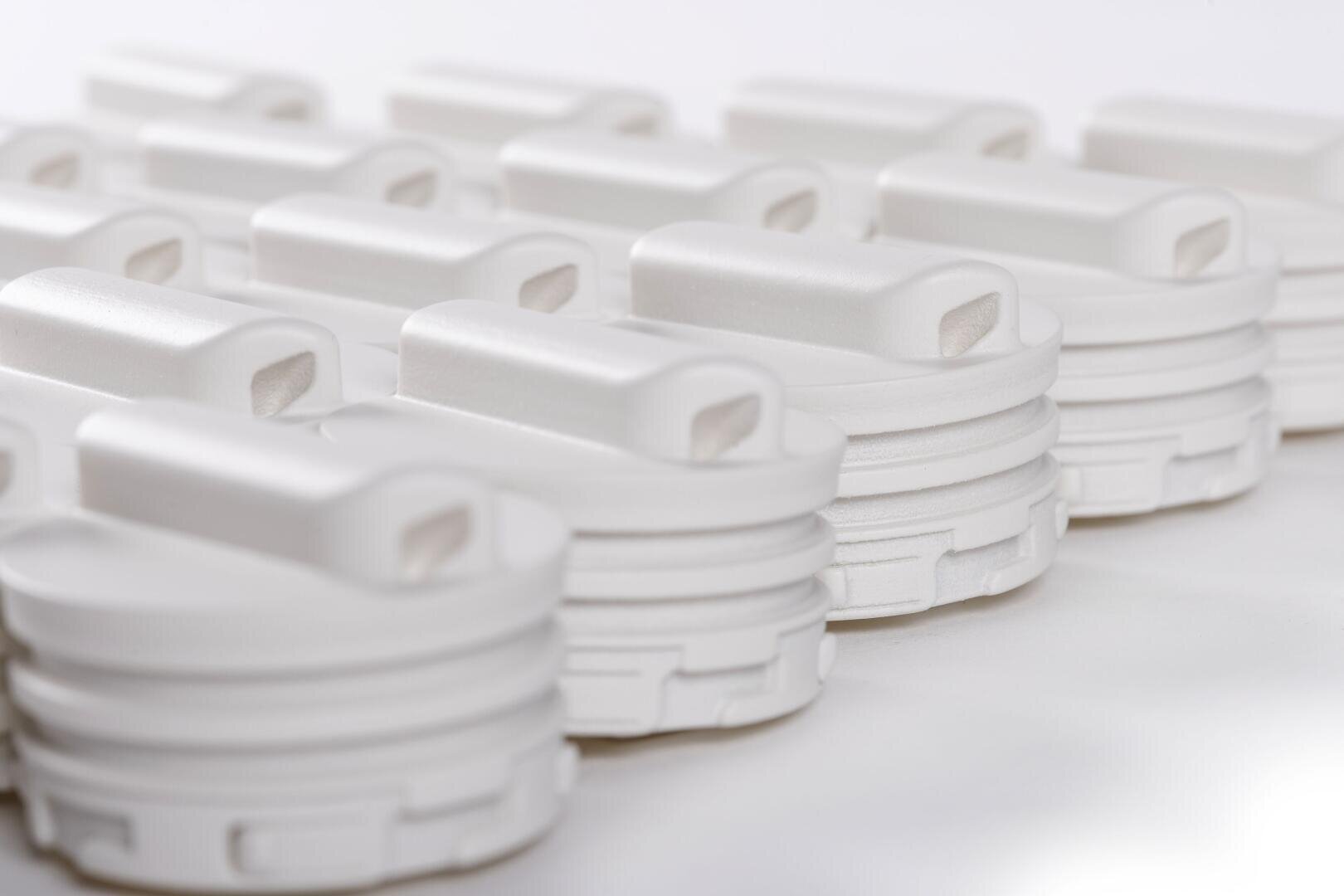 Rows of identical white plastic lids with rectangular openings are neatly arranged on a white surface, creating a pattern with soft shadows and lights.