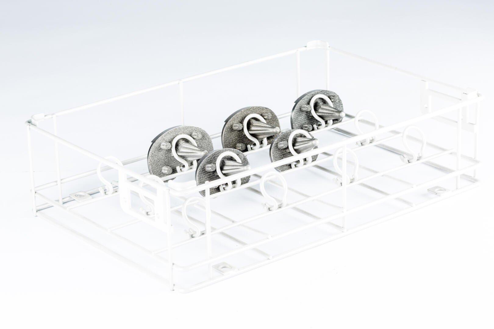 A white metal wire rack holds six round metal objects, each with a looped handle, arranged in two rows. The background is plain and white.