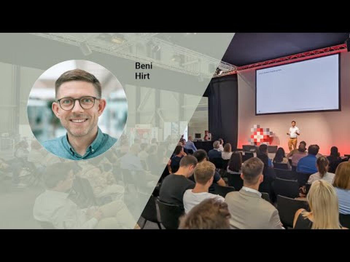 Ein Mann hält eine Präsentation auf der Bühne vor einem sitzenden Publikum in einem modernen Veranstaltungsraum. Der eingefügte Kreis zeigt ein Kopfbild eines lächelnden Mannes mit der Aufschrift Beni Hirt auf der linken Seite des Bildes.