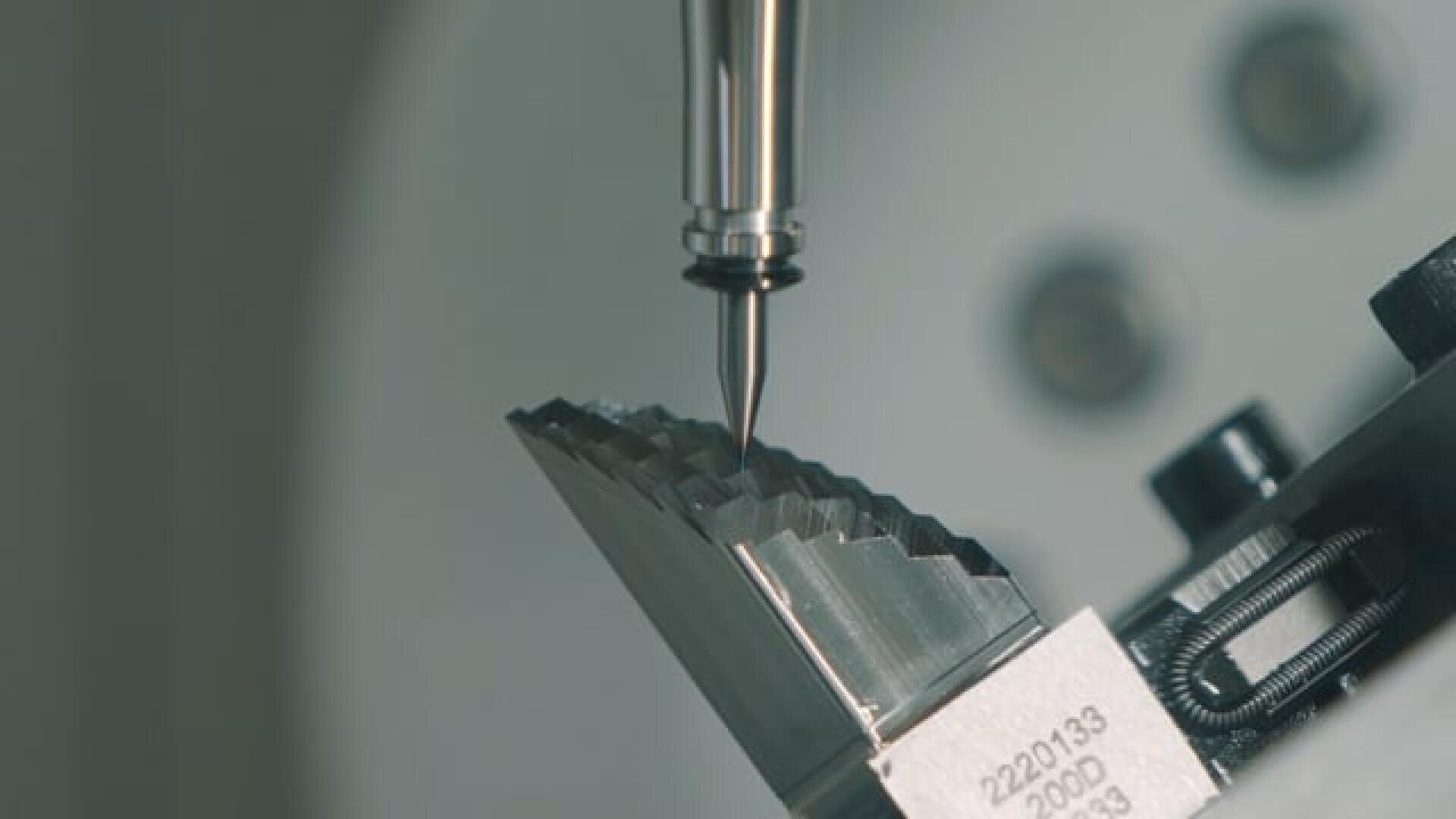 Close-up of a CNC machine tool precisely milling or drilling a metal, toothed component, with the detailed cutting tool engaging the edge of the metal part.