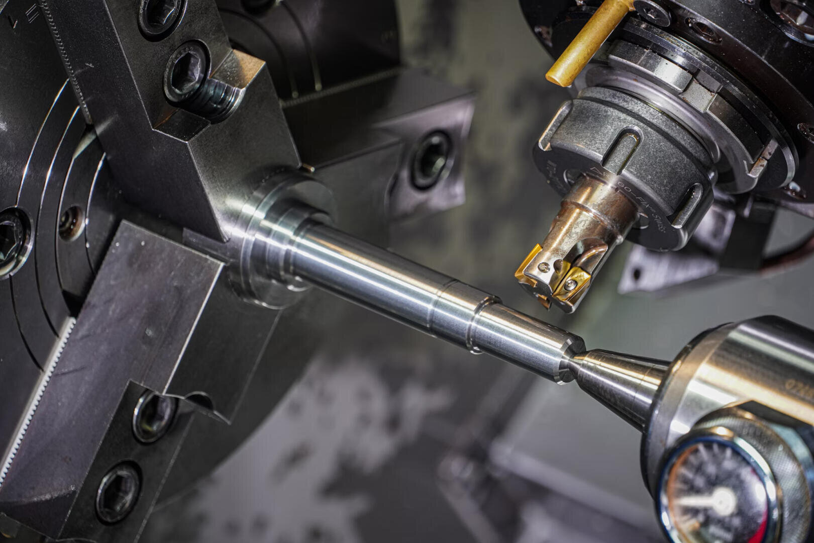 Nahaufnahme einer CNC-Drehmaschine bei der Bearbeitung einer Metallstange, wobei ein Schneidwerkzeug und ein Messgerät in der Nähe des rotierenden Werkstücks positioniert sind.