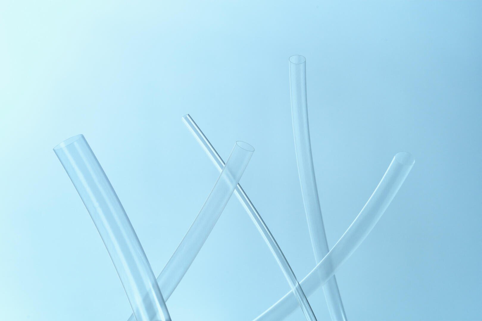 Mehrere transparente Kunststoffröhren sind aufrecht und diagonal vor einem hellblauen Hintergrund angeordnet, wodurch eine minimalistische und abstrakte Komposition entsteht.