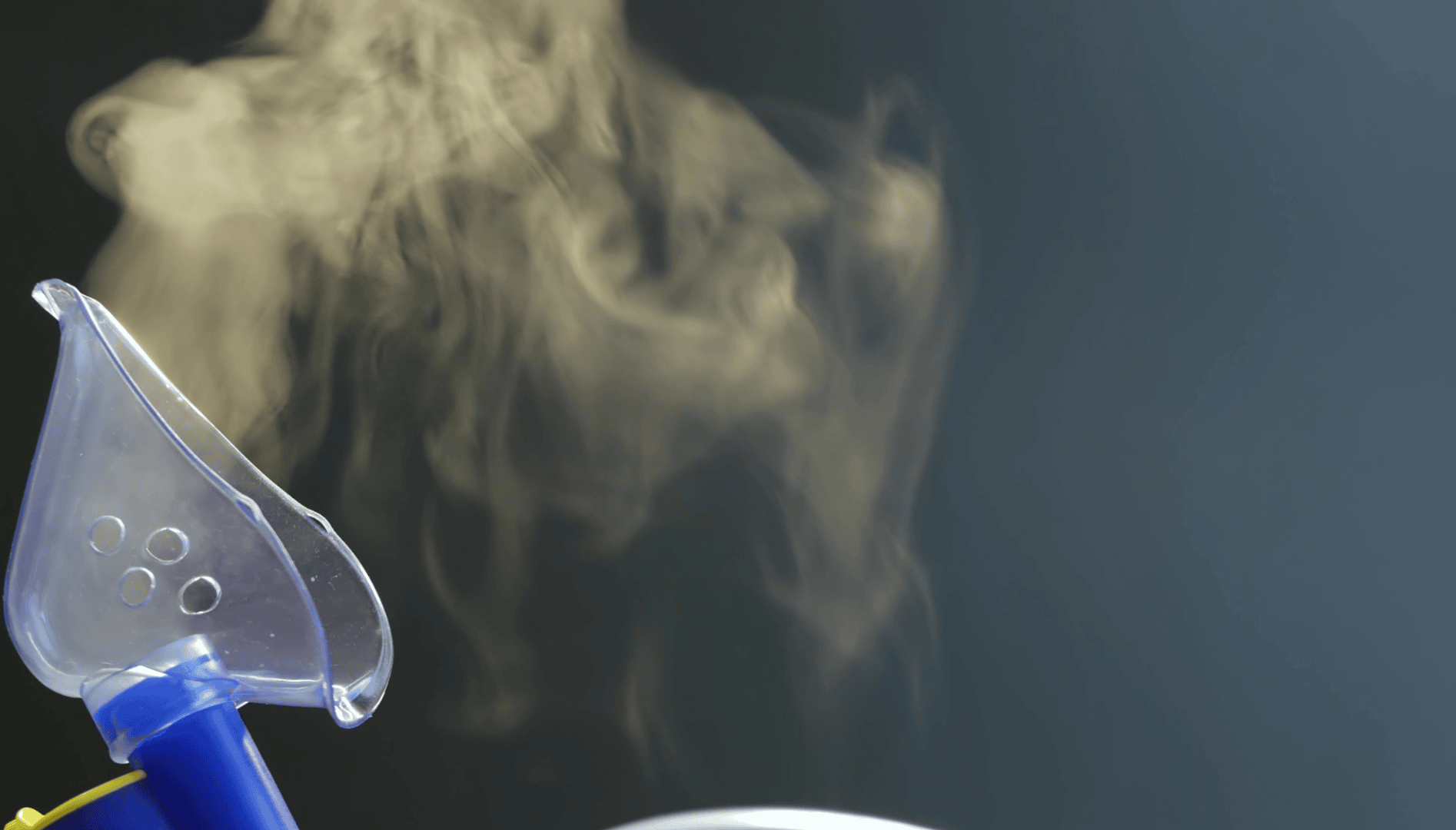 On the left is a transparent medical oxygen mask, on the right, clouds of steam rise against a dark background.
